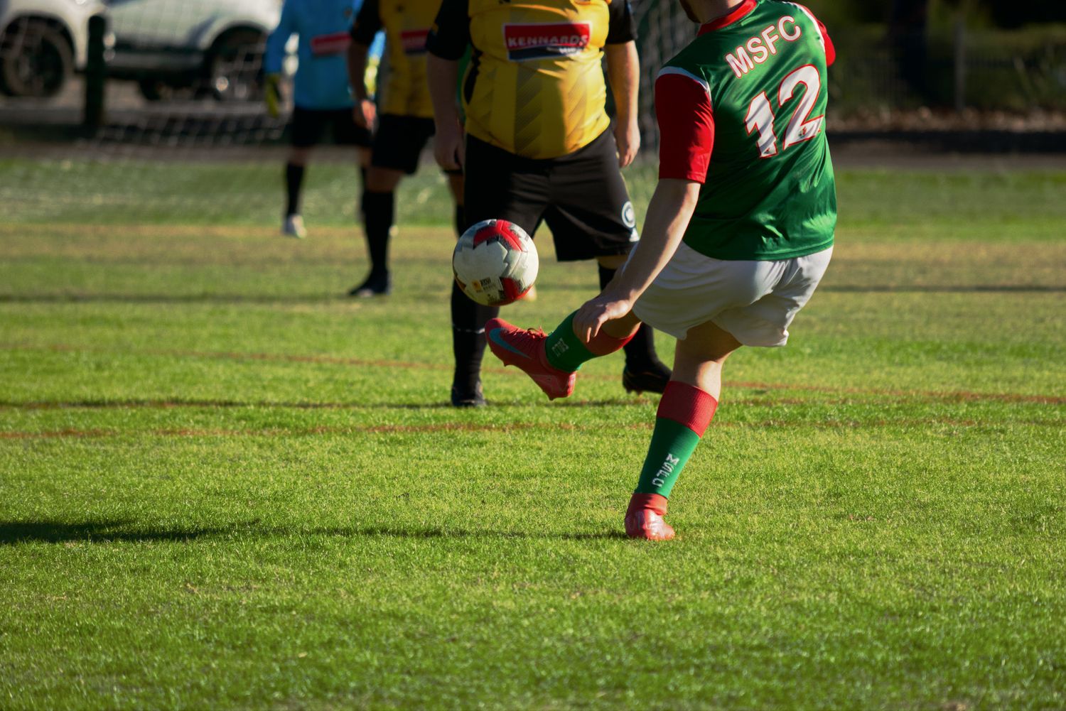 MSFC player number 12 kicks the ball on a bright green soccer field during a match.