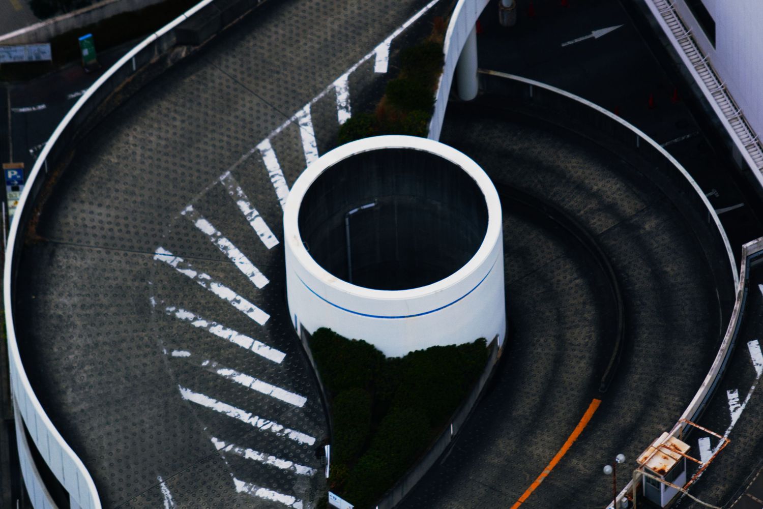 Aerial view of a white cylindrical structure centered in a spiral road with zebra crossing markings.