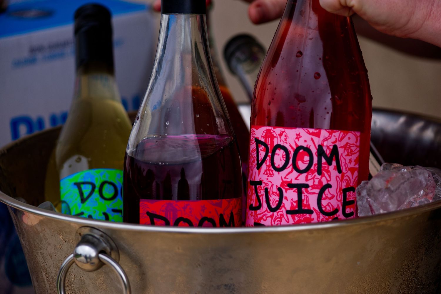 Three wine bottles labeled Doom Juice chilling in an ice bucket at a party.