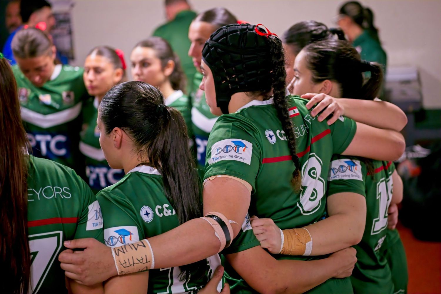 Female rugby league players in green jerseys huddle together in a show of team unity and support.