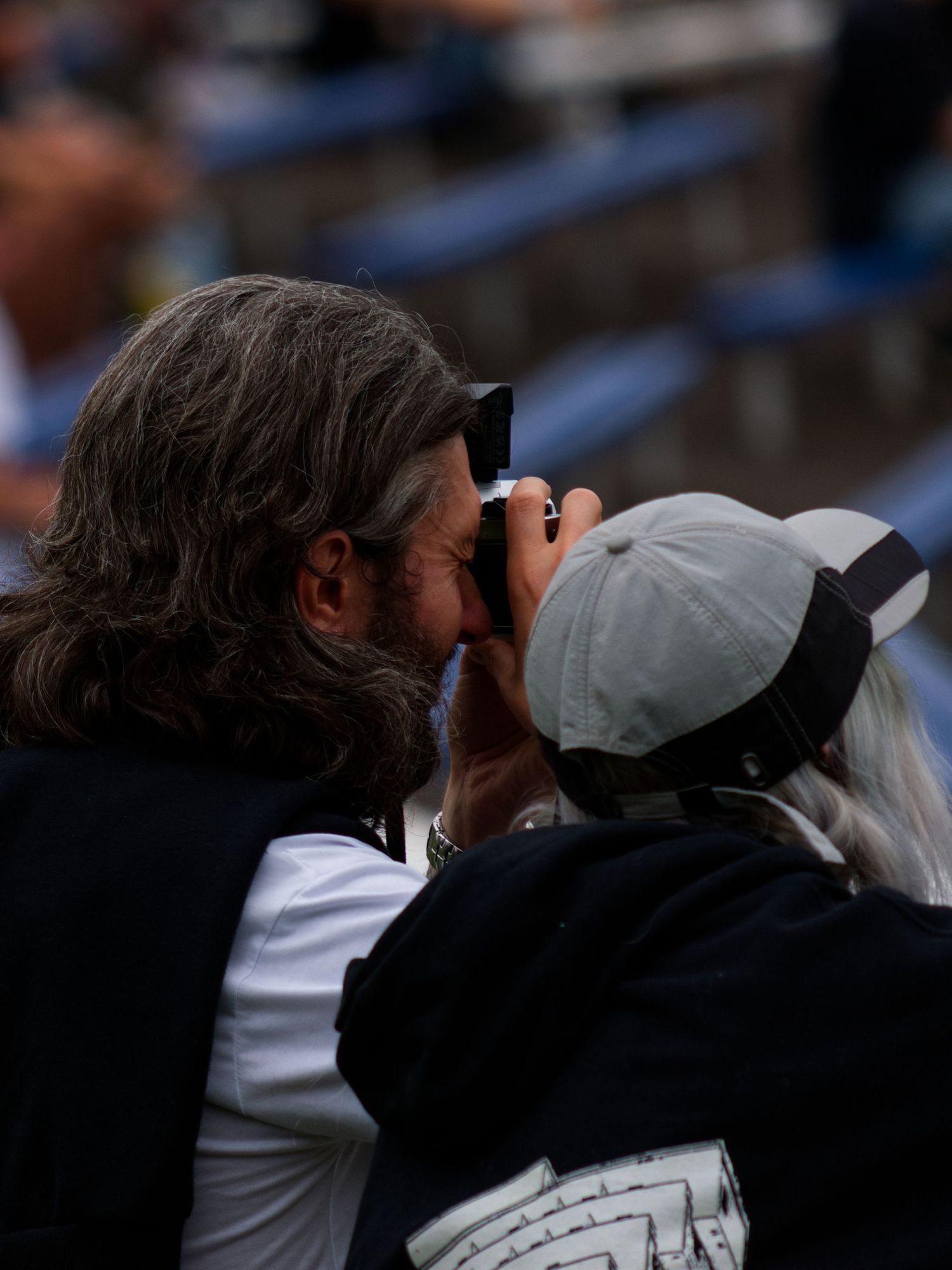 Long-haired man looking through camera at an outdoor sports event.