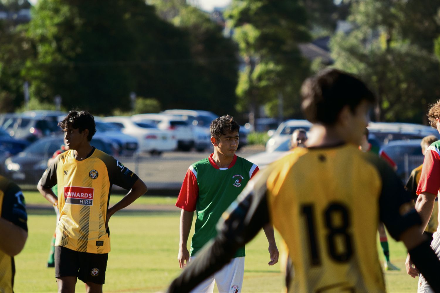 Soccer players in green and yellow jerseys stand on the field during an outdoor match.