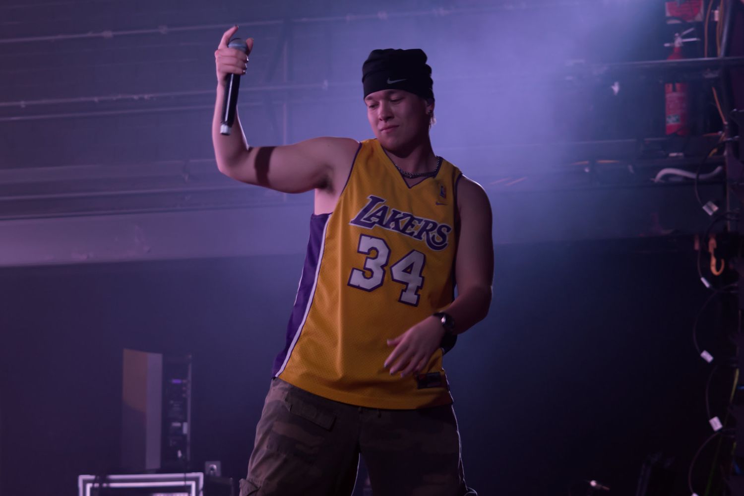 Energetic performer in Lakers 34 jersey holds microphone on smoky concert stage.