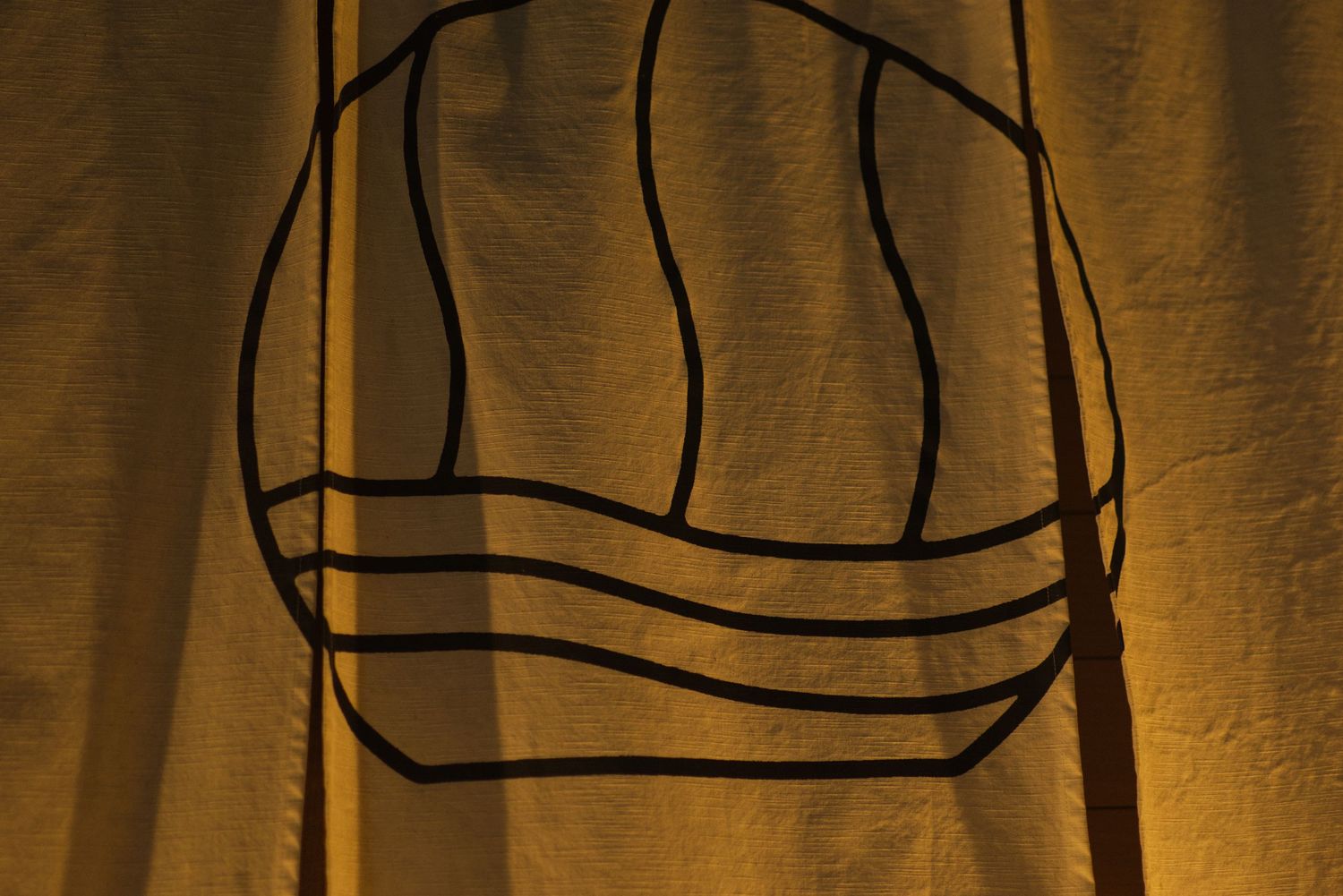 Shadow silhouette of a logo cast on golden yellow fabric curtain background.