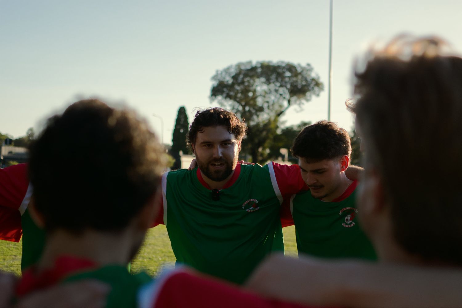 Soccer players in green and red uniforms huddle together on a field before a match.