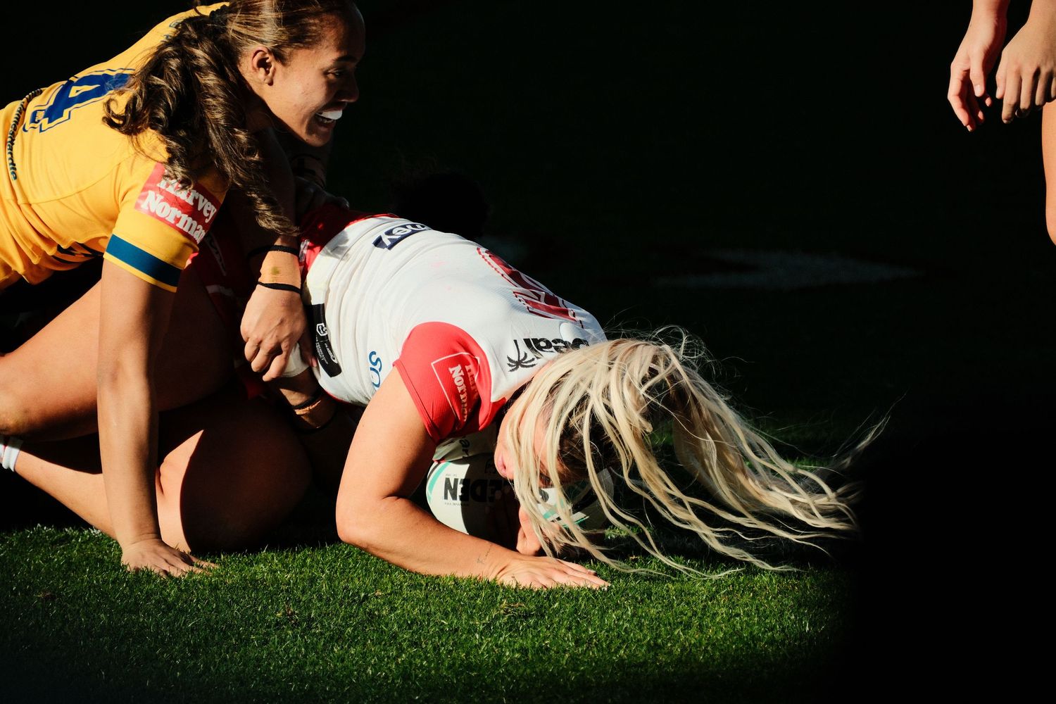 Female rugby player scoring a try on green grass field during a competitive match.