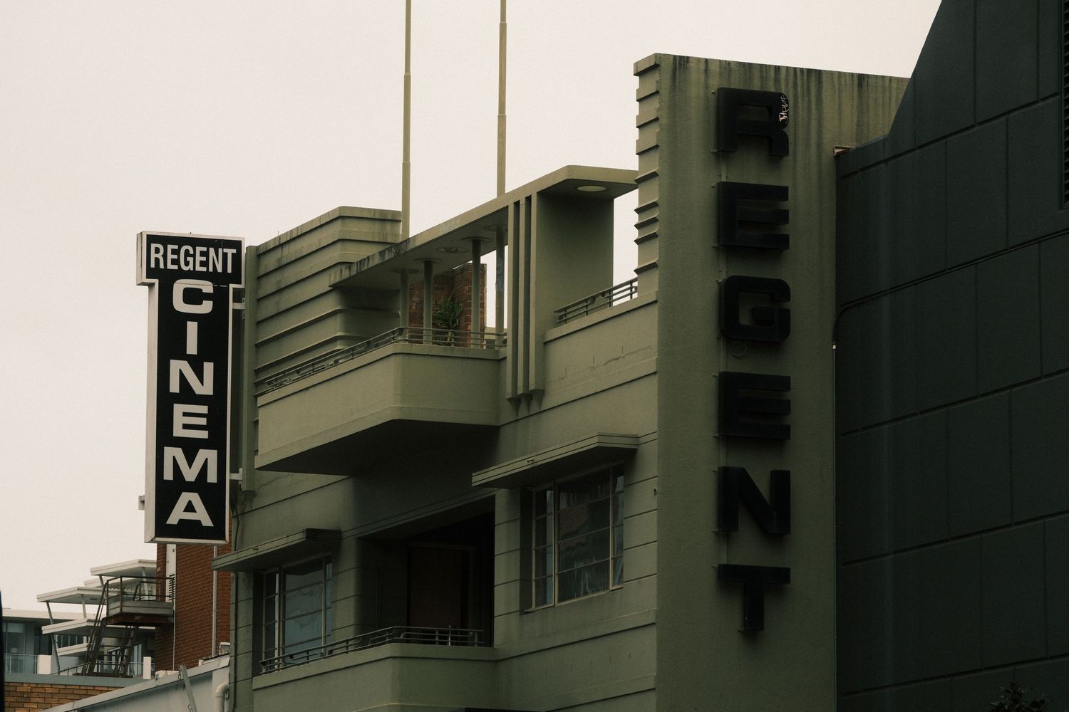 Art Deco Regent Cinema building exterior with vertical neon sign and bold lettering on gray facade.