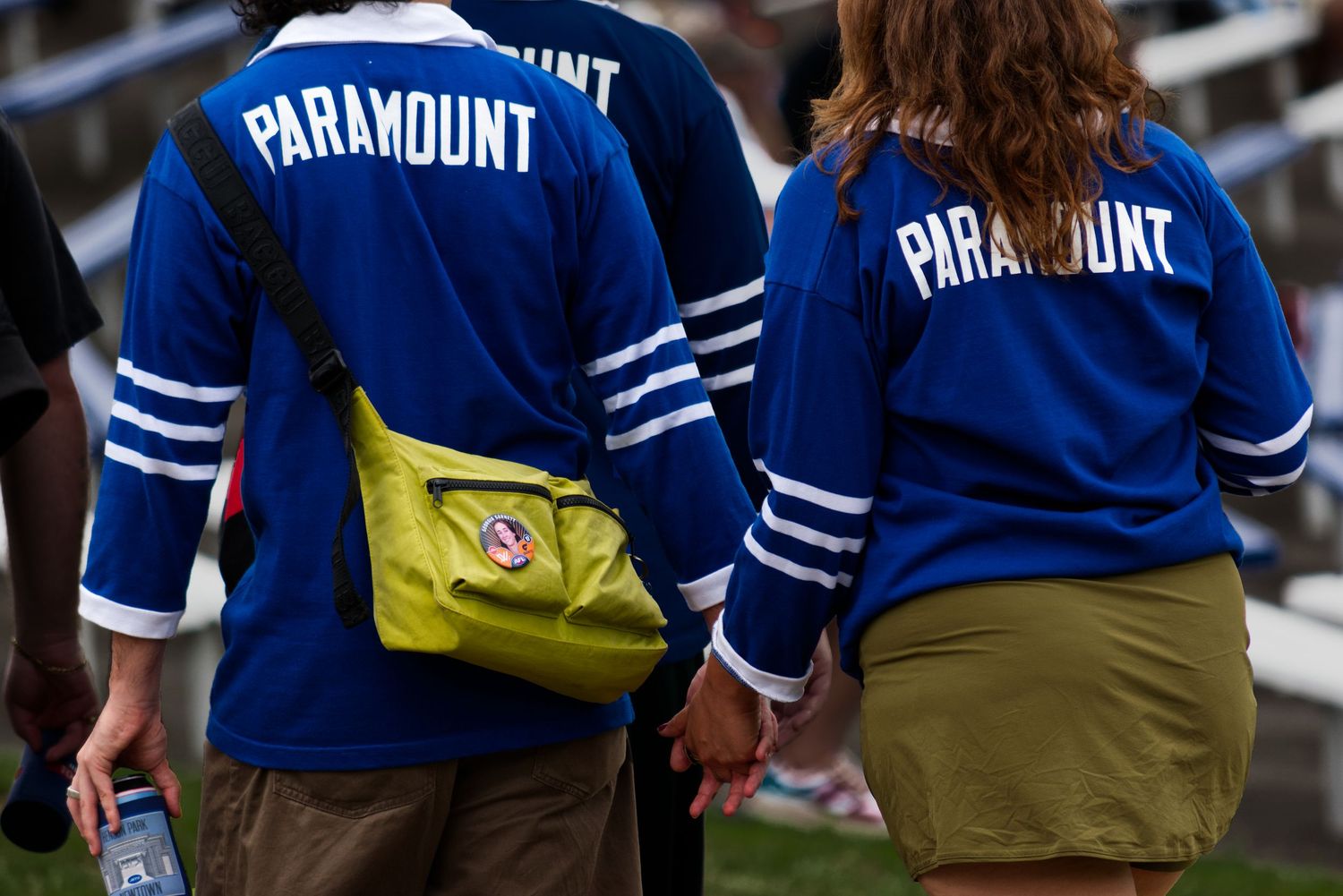 Two people wearing matching blue Paramount jerseys hold hands at an outdoor event.