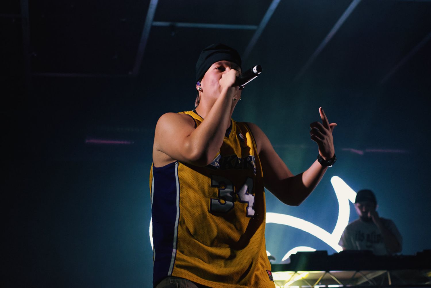 Young male rapper performing on stage wearing a yellow basketball jersey under blue stage lights.