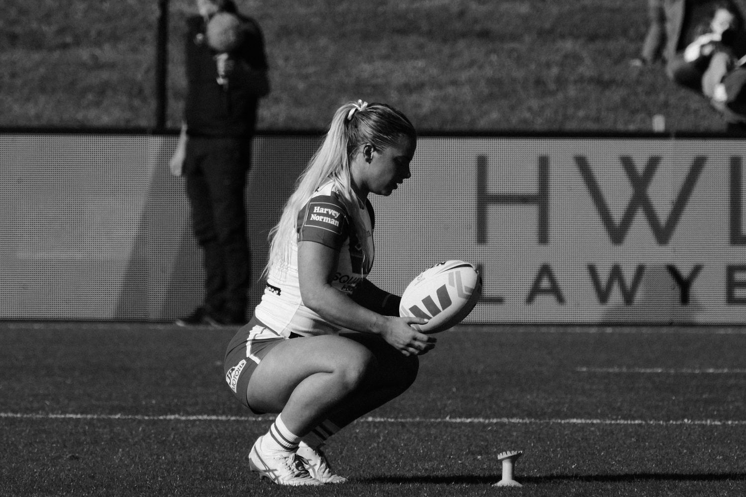 Female rugby player crouching to place ball on tee during a match, black and white sports photography.