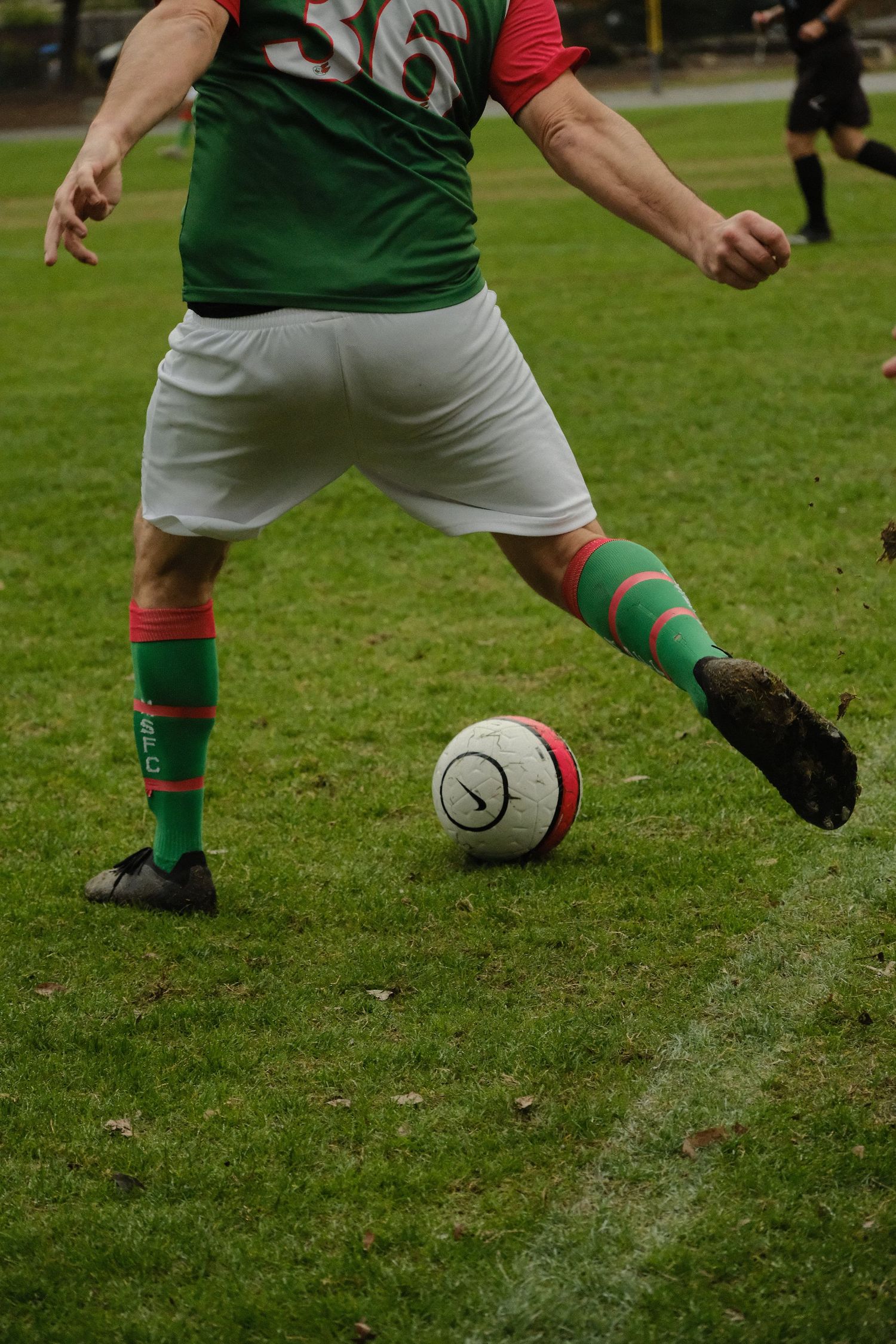 Soccer player in green and red uniform kicking a ball on a grass field.