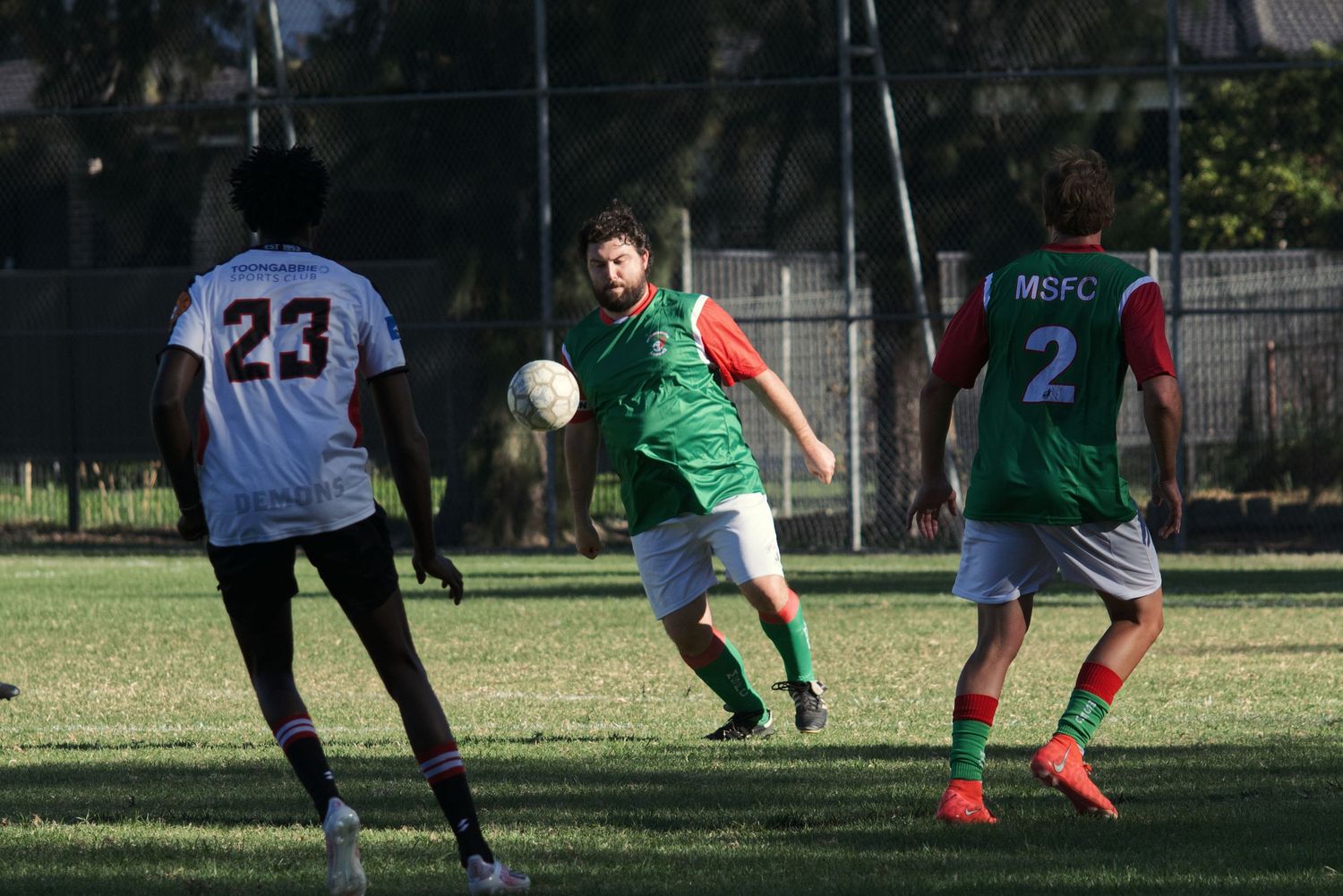 Soccer players in green MSFC jerseys pass the ball during a competitive outdoor match on grass.