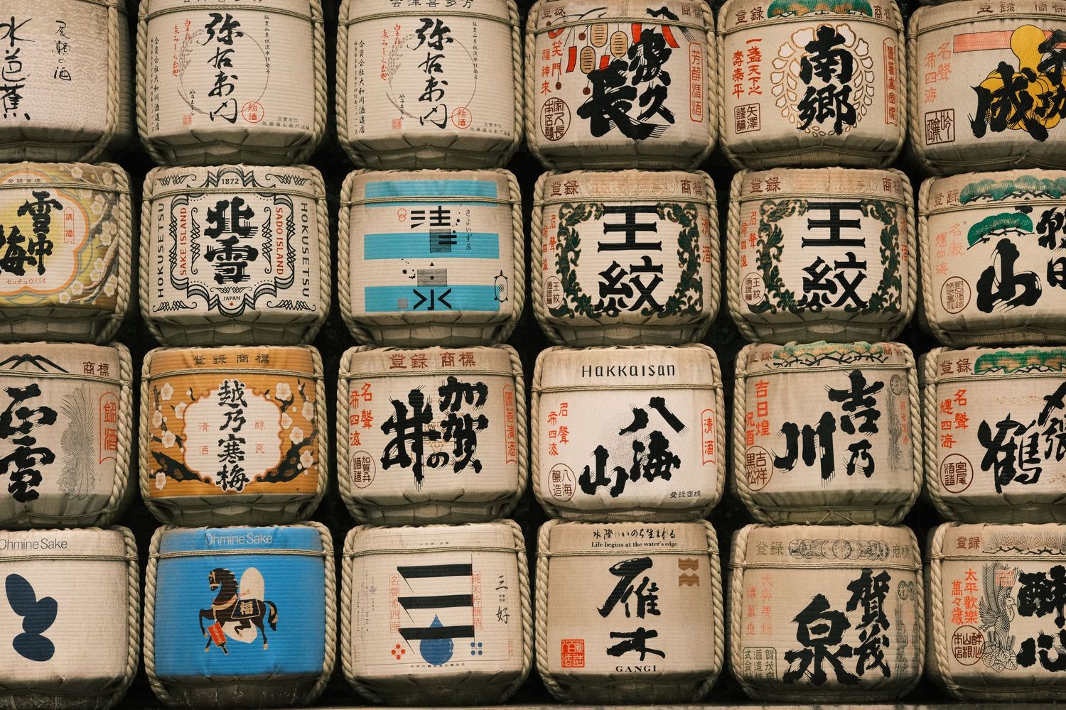 Rows of traditional Japanese sake barrels wrapped in straw with colorful kanji calligraphy on display.