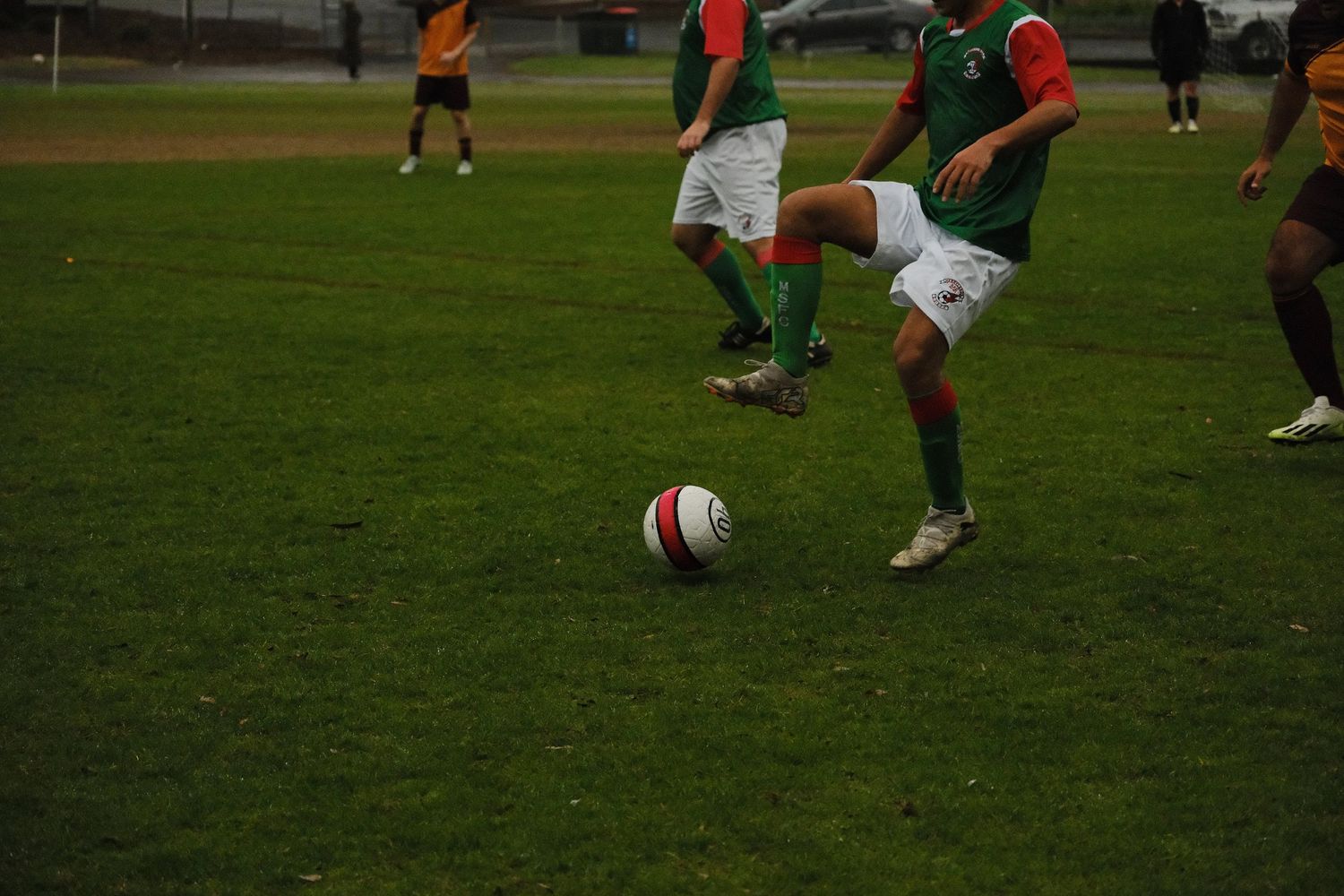 Soccer players in green uniforms dribbling a ball on a grass field during a game.