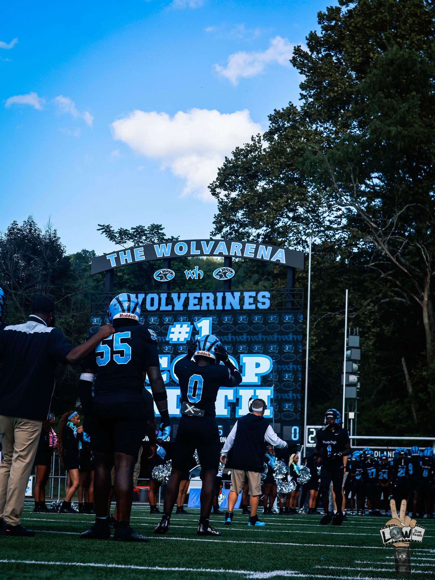 Football players walk toward the Wolverines Wolvarena stadium entrance under a blue sky.