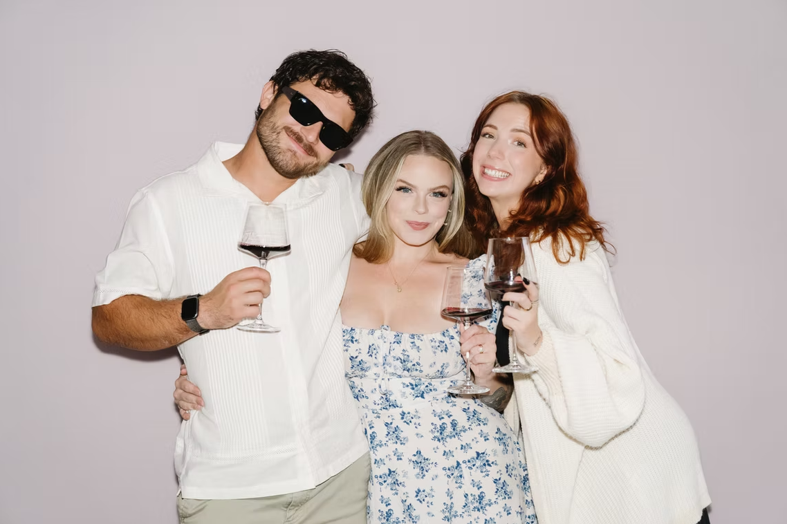Group of three holding up wine glasses in photo booth.