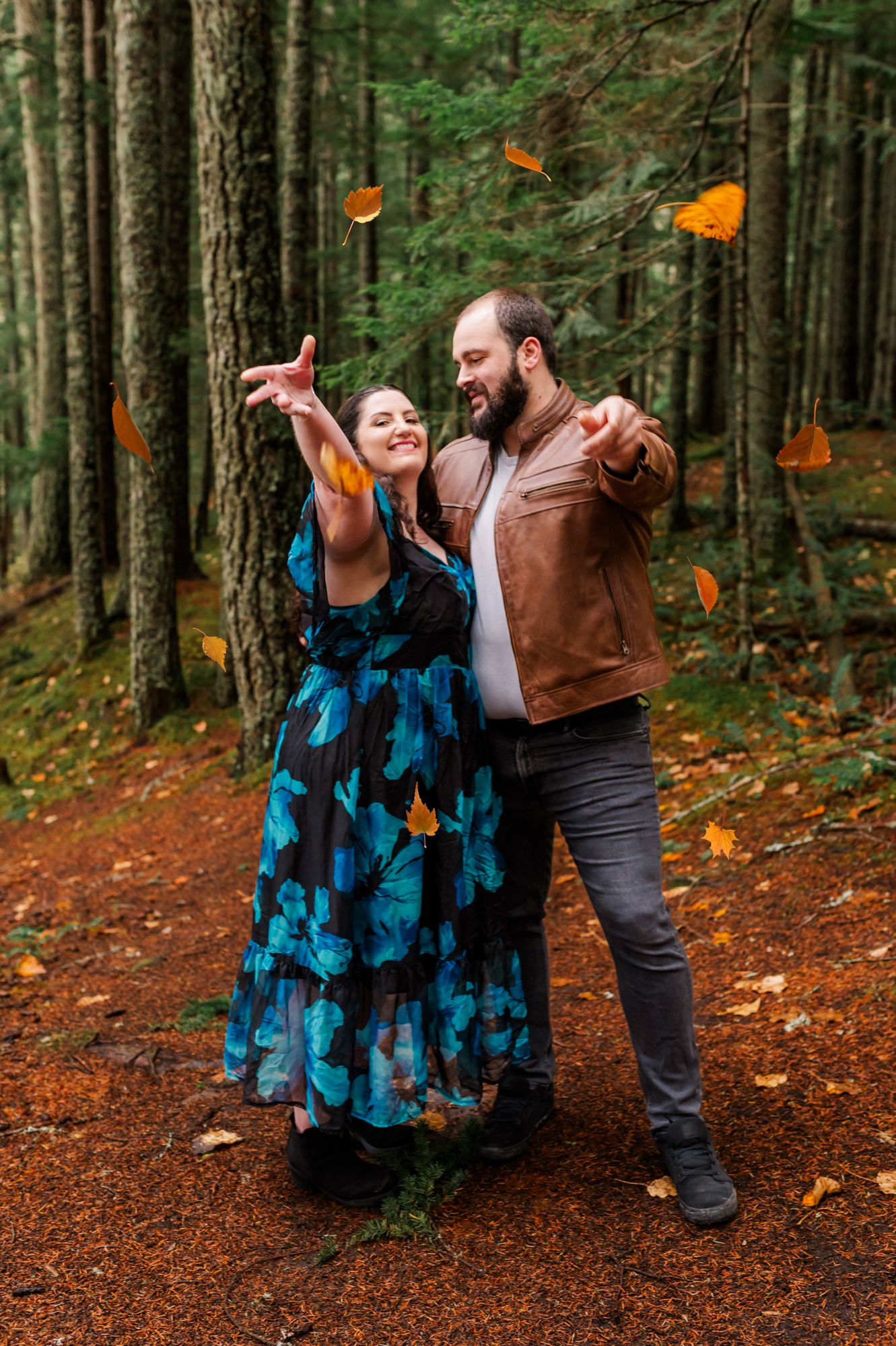 Couple laughing and tossing autumn leaves in a forest, wearing a floral dress and brown leather jacket at Chilliwack Lake Regional Park.