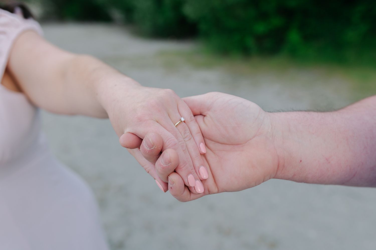 Two people holding hands tenderly, one wearing a gold ring, with a soft blurred green background in The Fraser Valley.