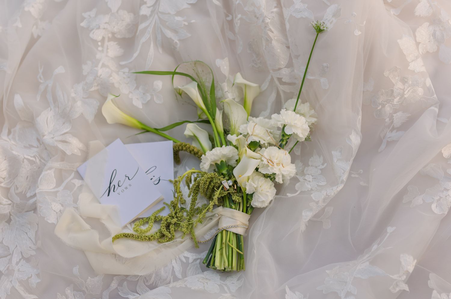 White Fraser Valley wedding bouquet with calla lilies and roses on lace bridal gown with calligraphy card.