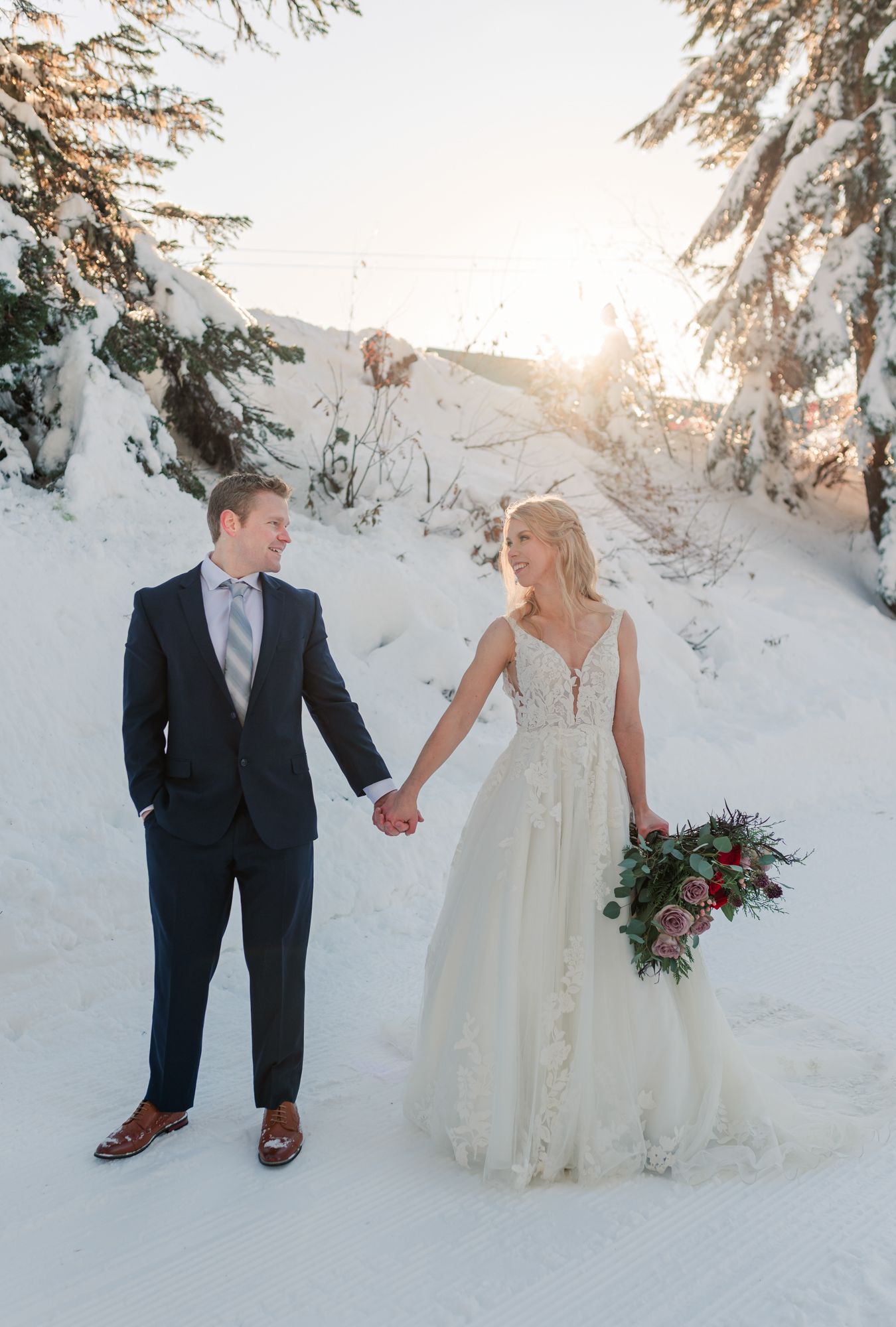 Grouse Mountain wedding bride and groom holding hands, bride holding red and pink bouquet, groom in navy suit.