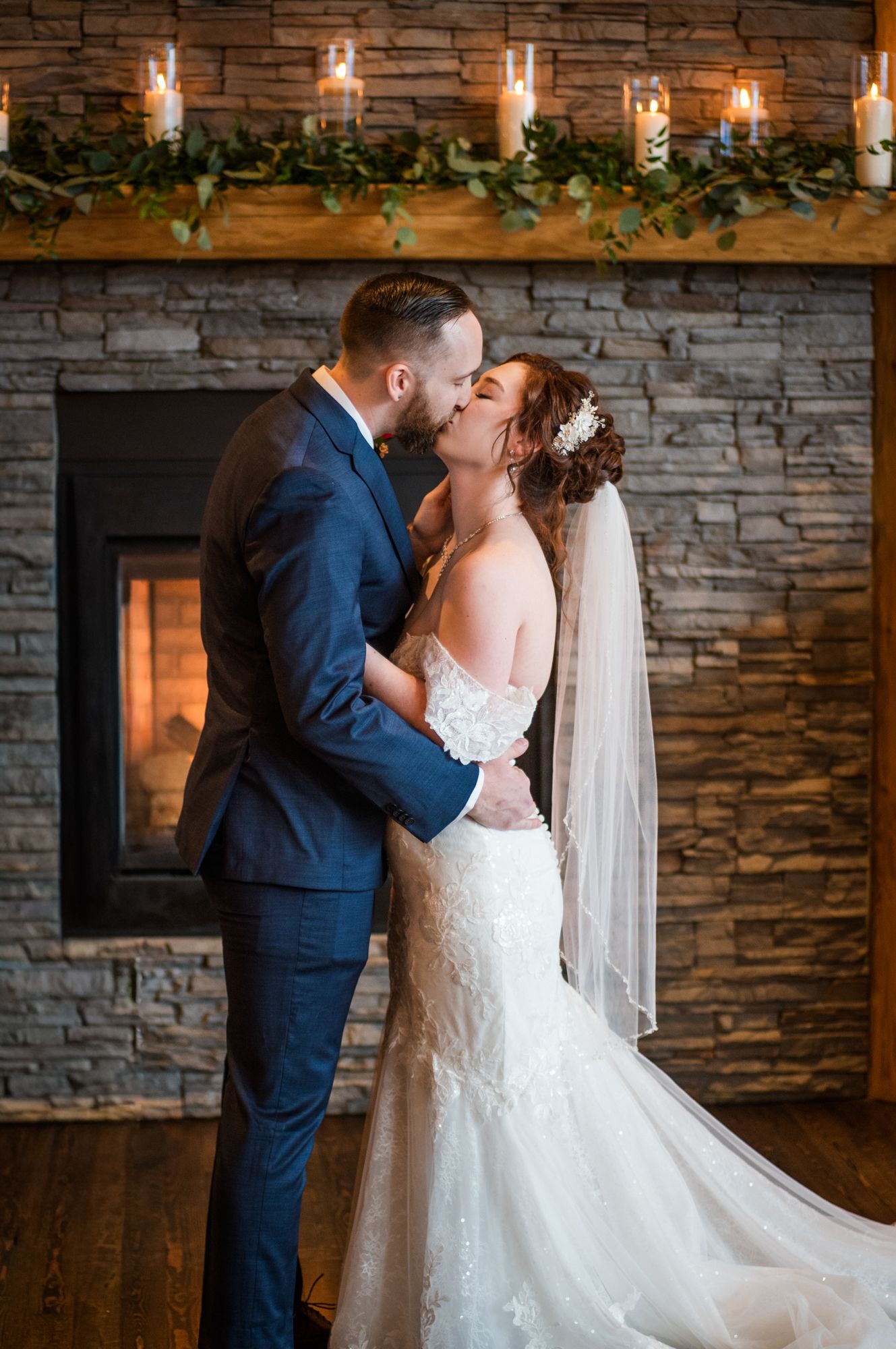 Bride and groom share a romantic kiss in front of a stone fireplace adorned with candles at Fraser River Lodge Venue.