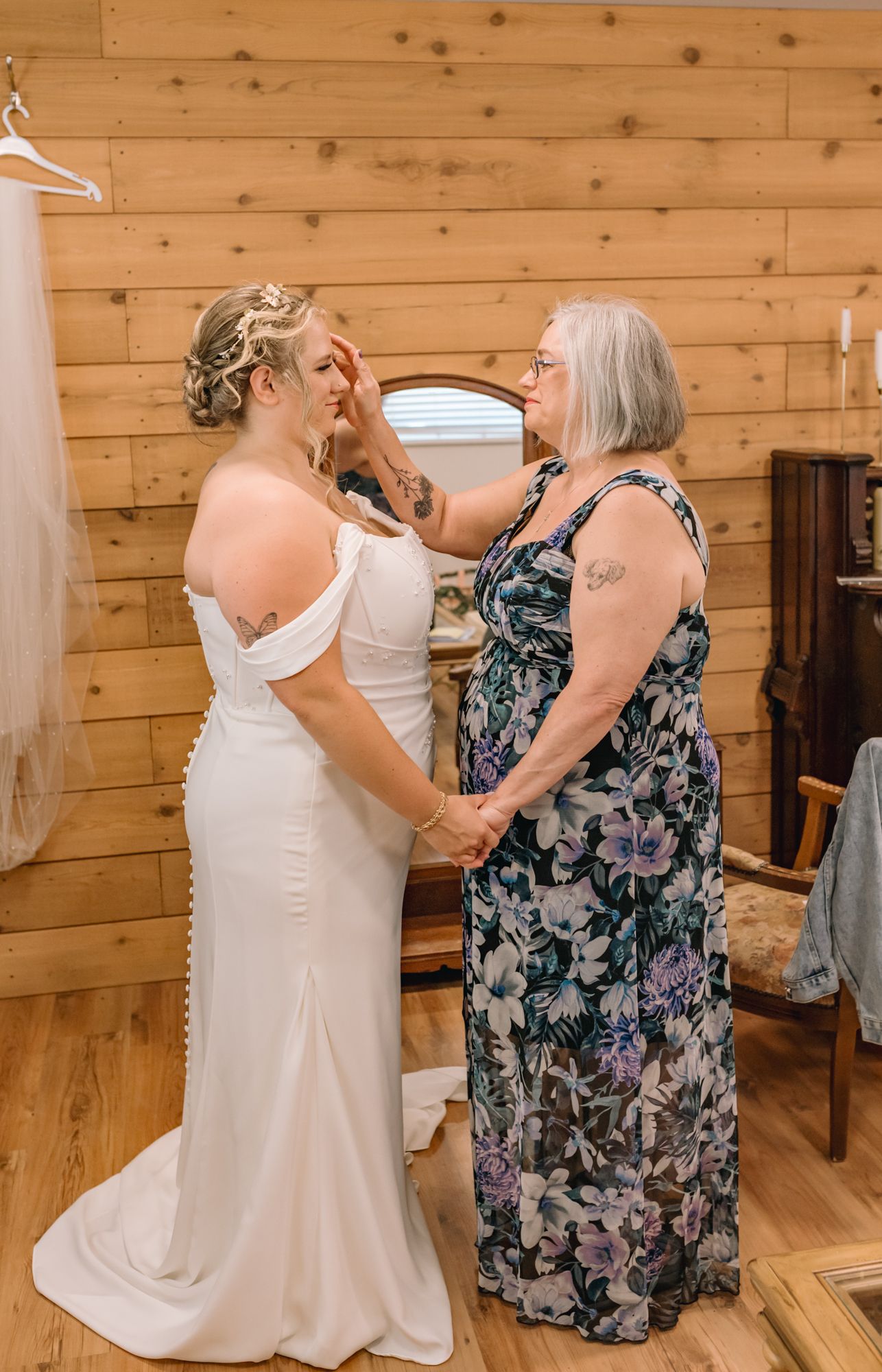A bride in a white gown holds hands with an older woman in a floral dress in a rustic wood-paneled bridal room in Langley, BC.