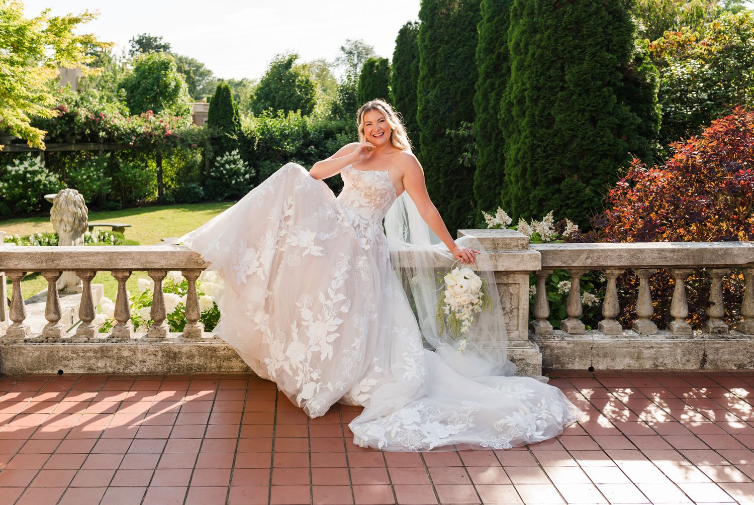 Bride in floral lace ballgown twirling on stone terrace surrounded by lush garden greenery at Hycroft Manor in Vancouver, BC.