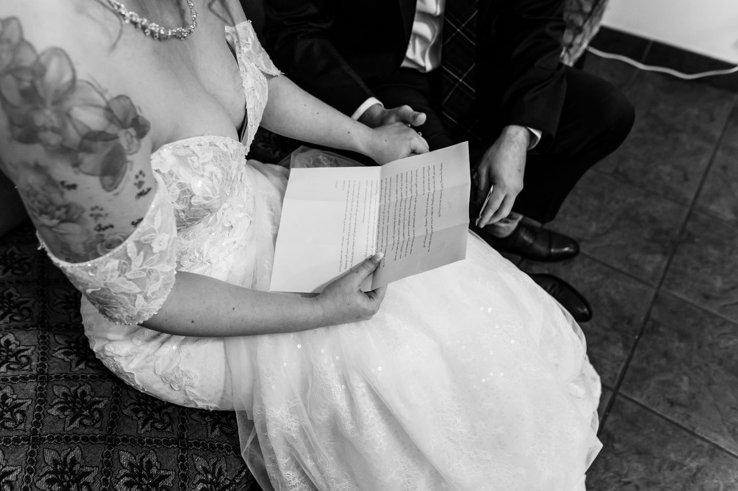Black and white wedding photo of bride in lace dress reading vows, groom seated beside her at their Fraser Valley wedding.