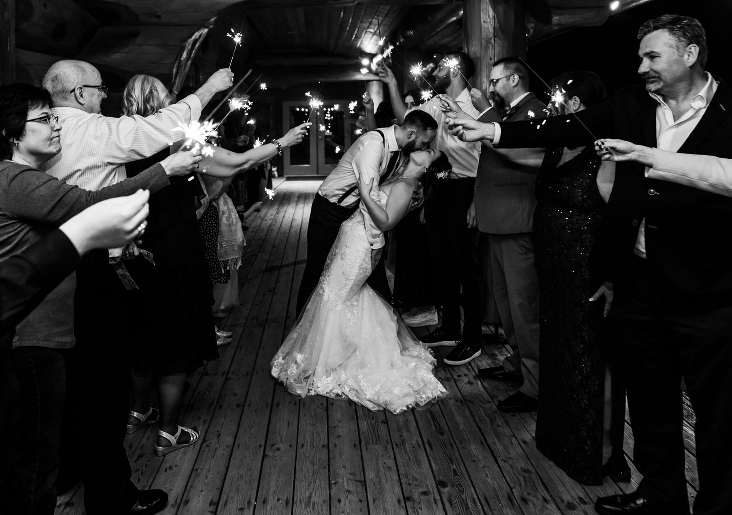 Black and white wedding photo of couple kissing under sparklers held by guests during romantic sendoff at Fraser River Lodge in Chilliwack.