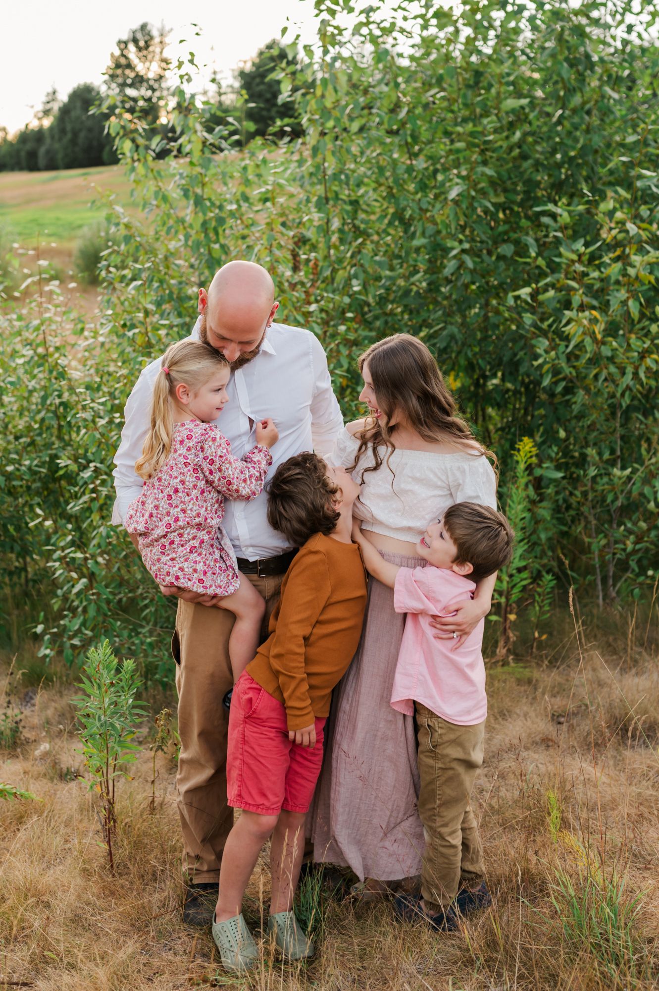 A loving family of five embraces outdoors in a field, with parents holding children in warm, earthy tones in Abbotsford, BC.