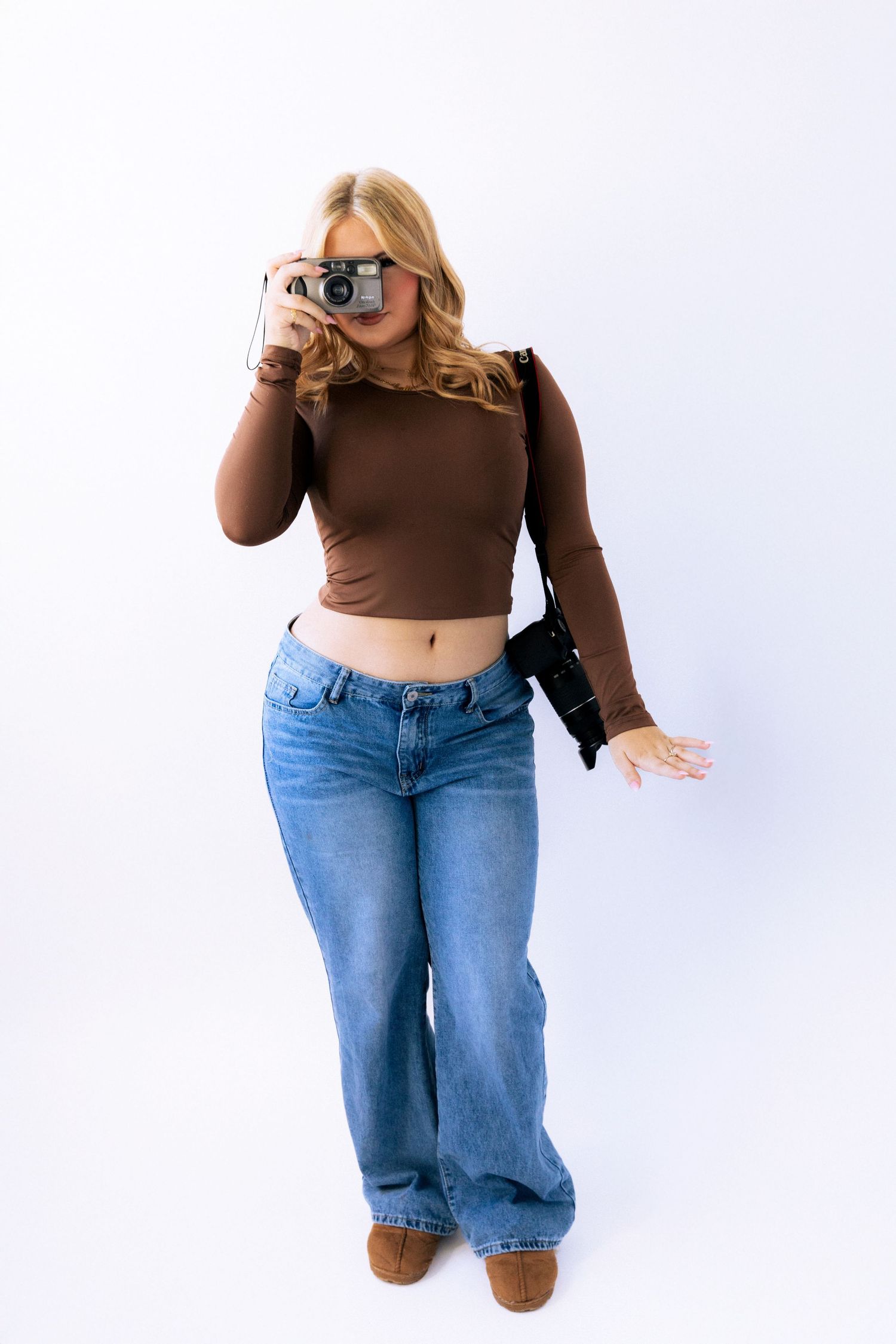 Casual outfit featuring a brown cropped long sleeve top paired with relaxed fit blue jeans and brown boots against white background.