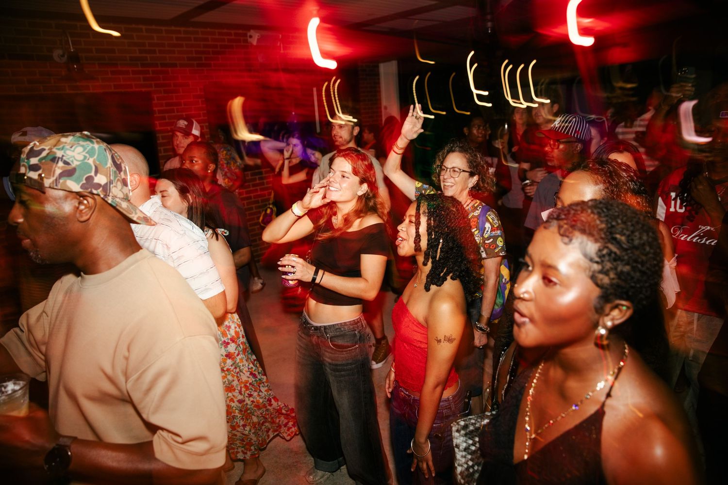 Nightclub scene with red lighting and people dancing on a crowded dance floor.