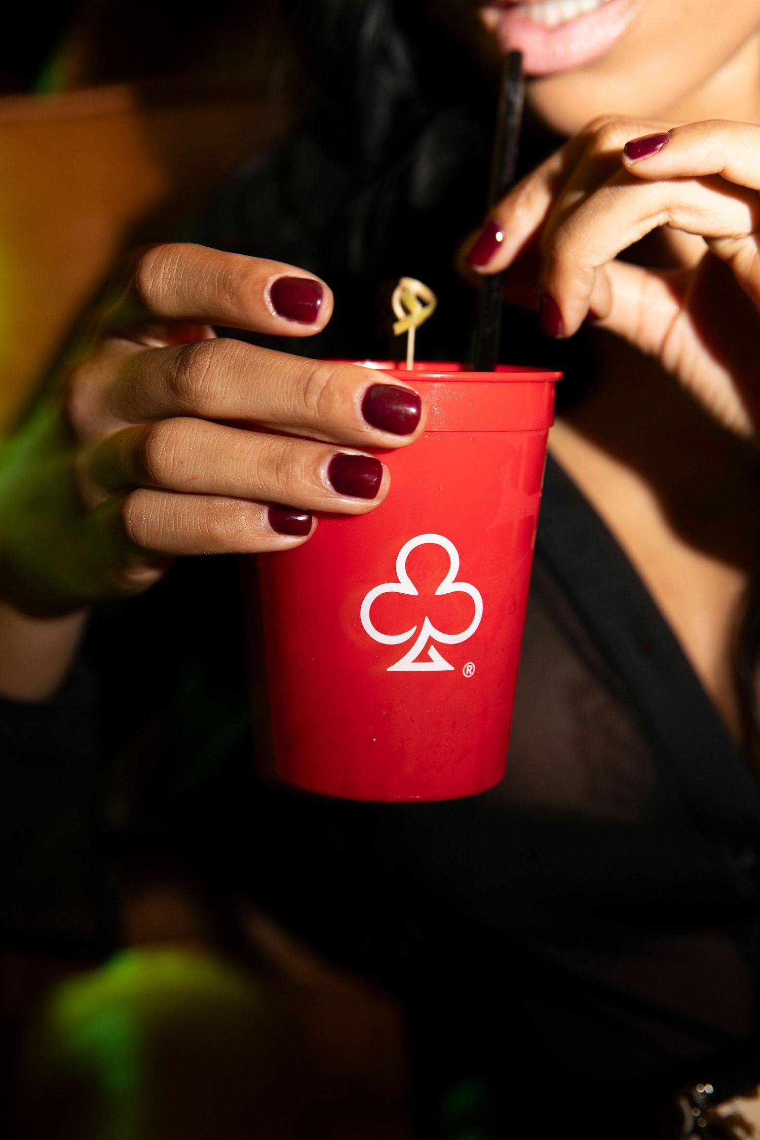Close-up of hands with burgundy nail polish holding red playing card themed cups in sequence.