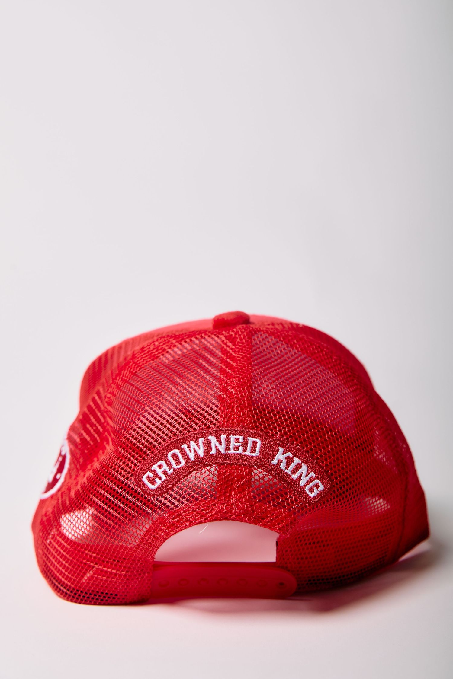 Red Crowned King mesh trucker hat shown from the back, featuring embroidered white logo text on a snapback cap.