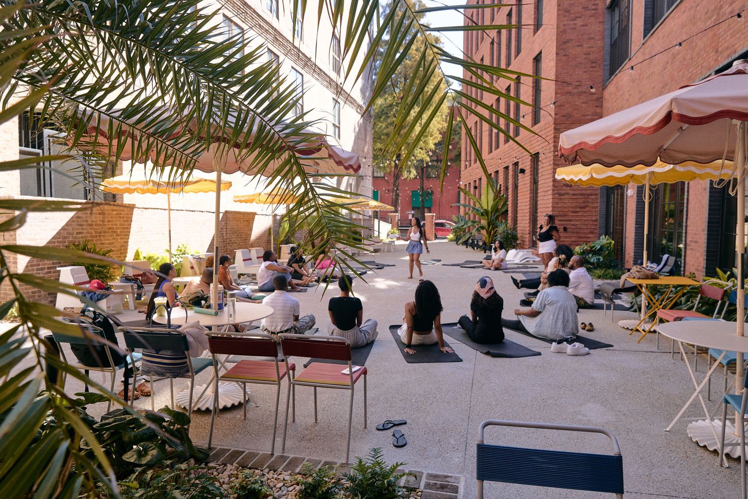 Outdoor dining area with tables and chairs set up near brick building with palm trees.
