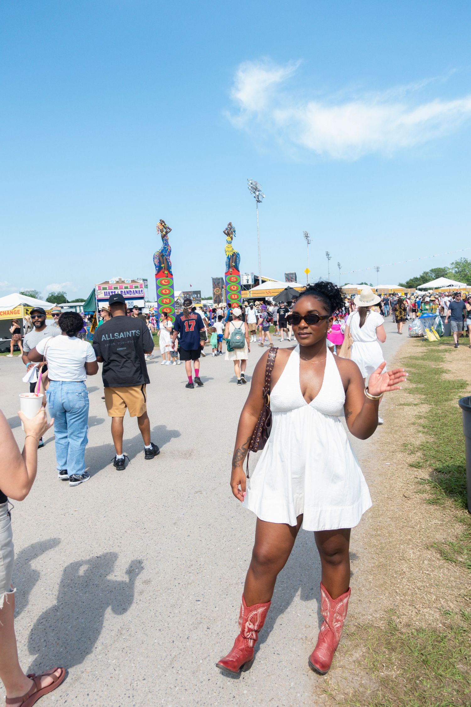 Festival attendees enjoy a sunny day at an outdoor event with colorful decorations and vendor stalls visible in the background.