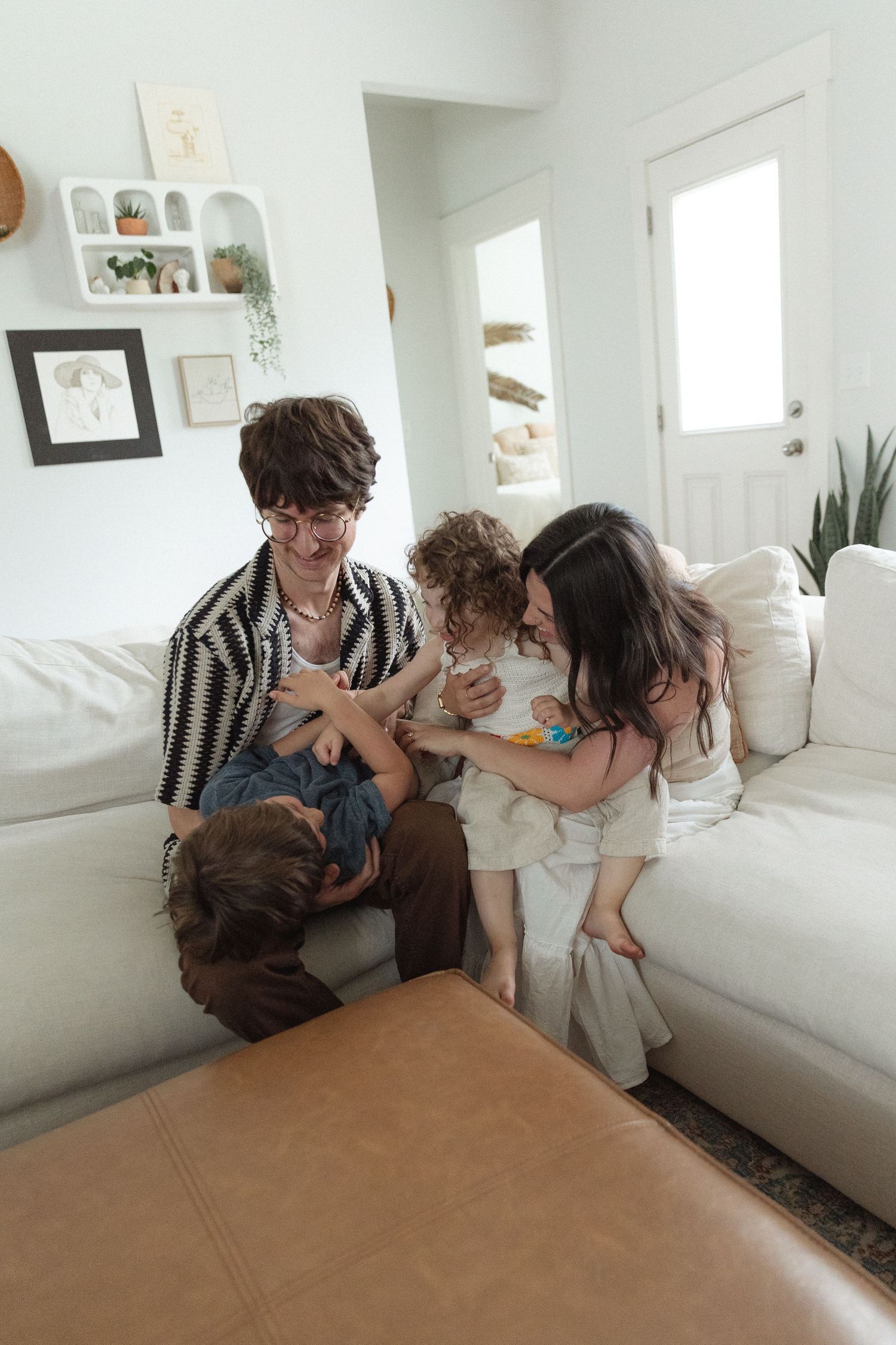 Family of four relaxing and playing together on a white couch in a bright modern living room.