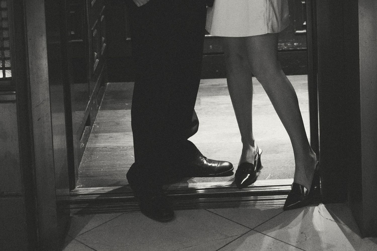 Black and white photo of couple standing in doorway showing only their legs and feet.