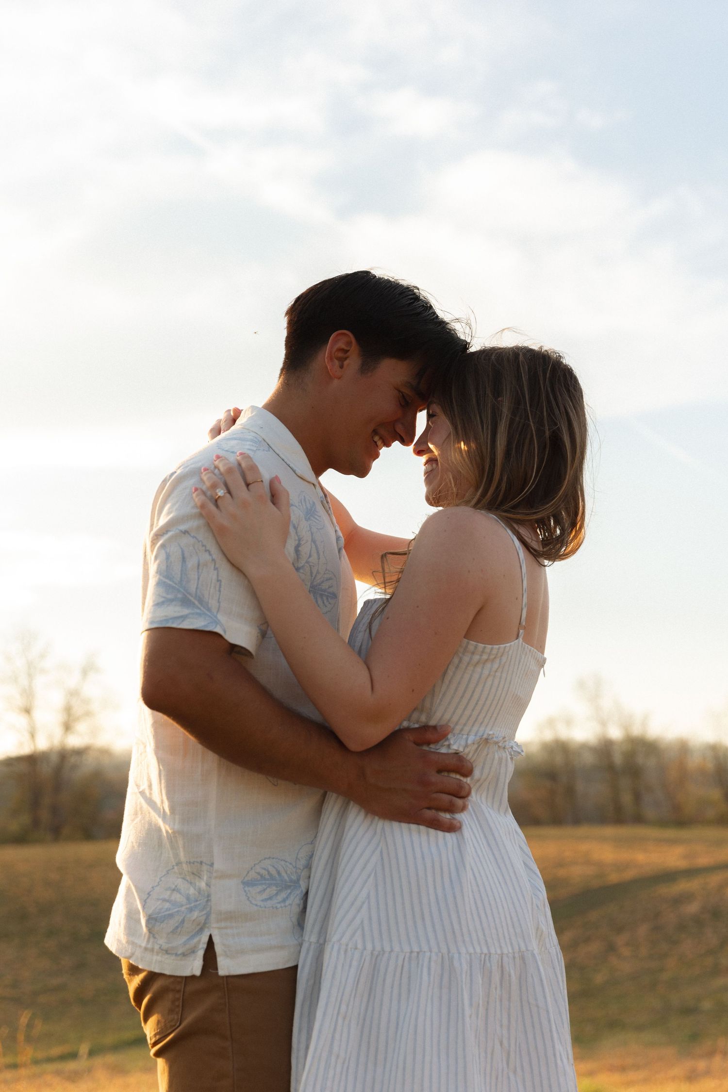 Romantic couple embracing and touching foreheads in golden sunset light in an open field.