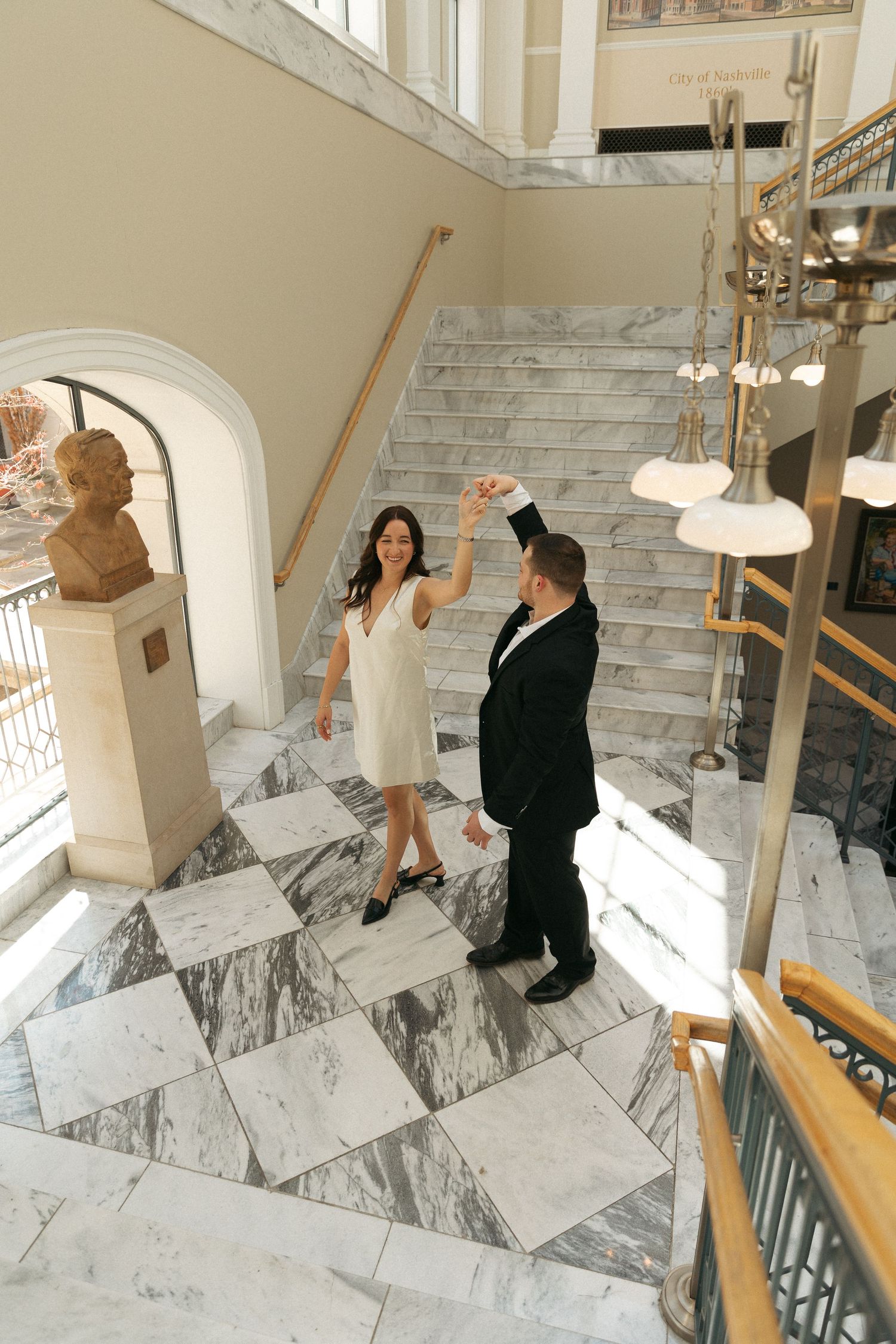 Couple dancing elegantly in a grand marble-floored building with a sweeping staircase.