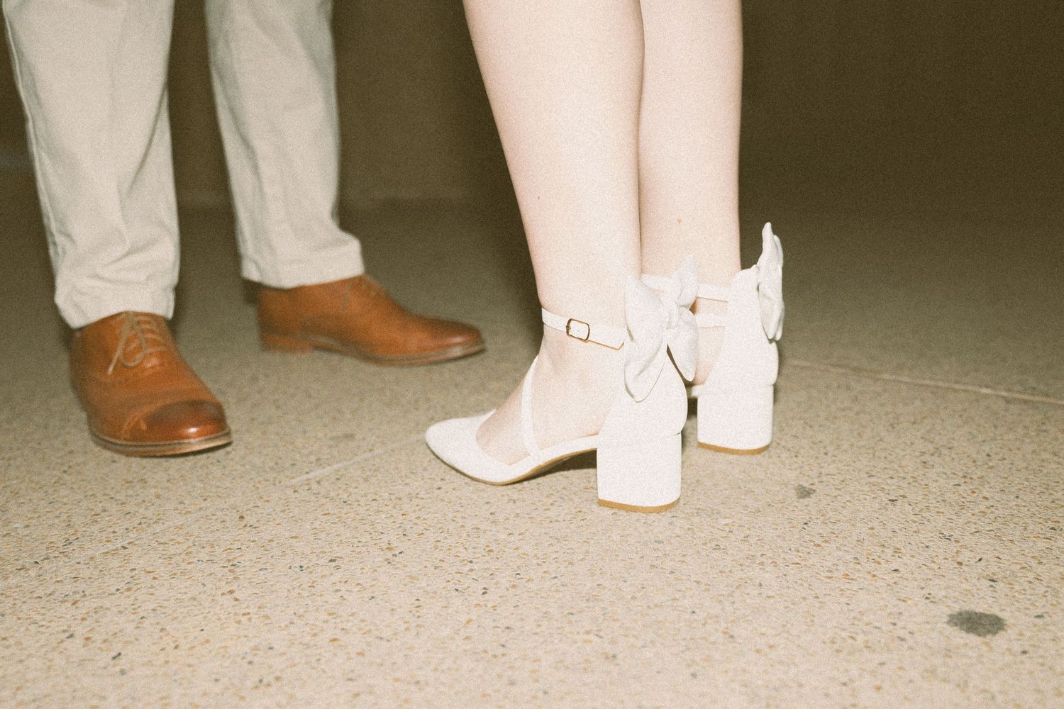 Close-up of wedding couple's shoes, brown leather oxfords and white block-heel ankle boots on concrete floor.
