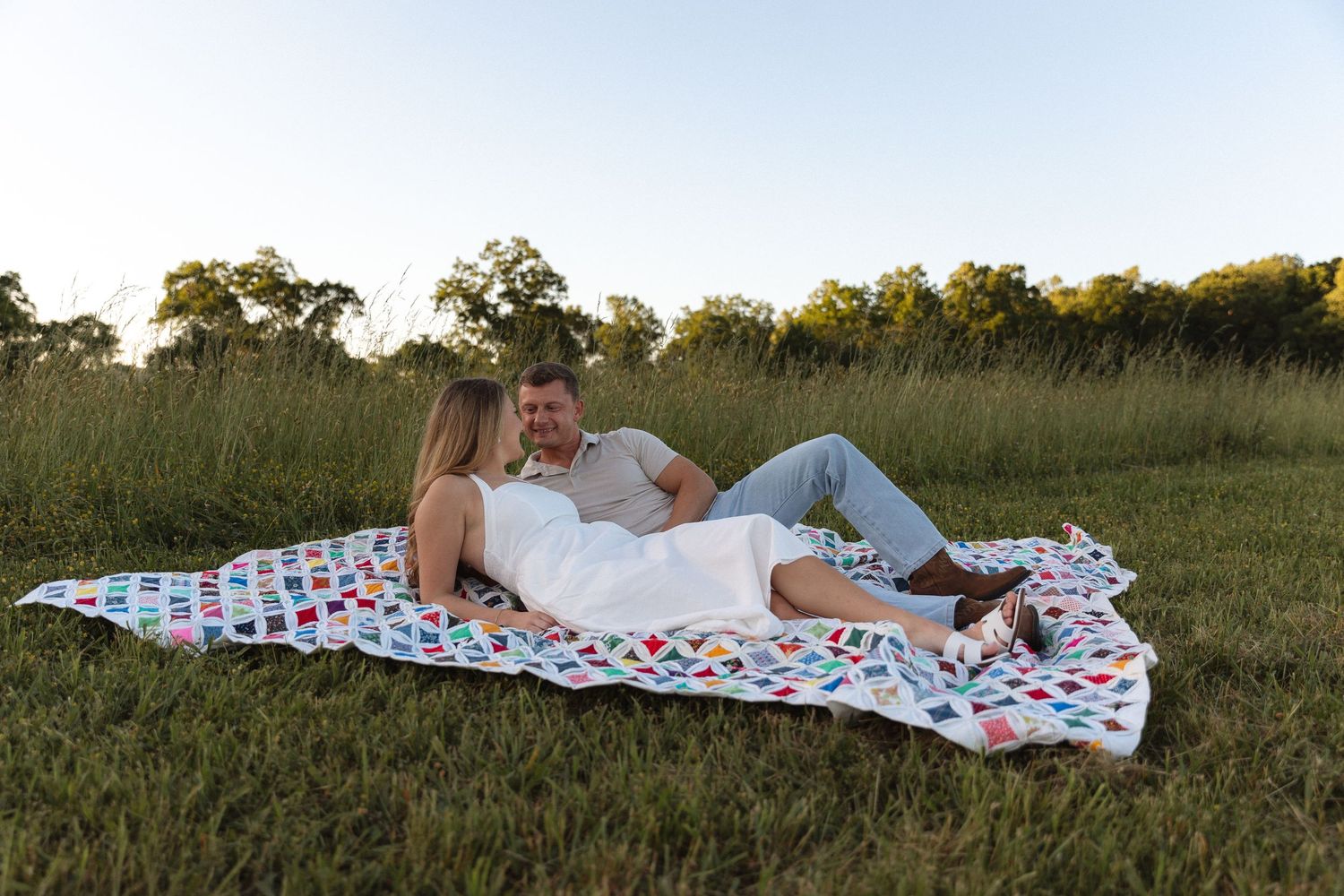 Couple relaxing together on a colorful blanket in a peaceful grassy field at sunset.