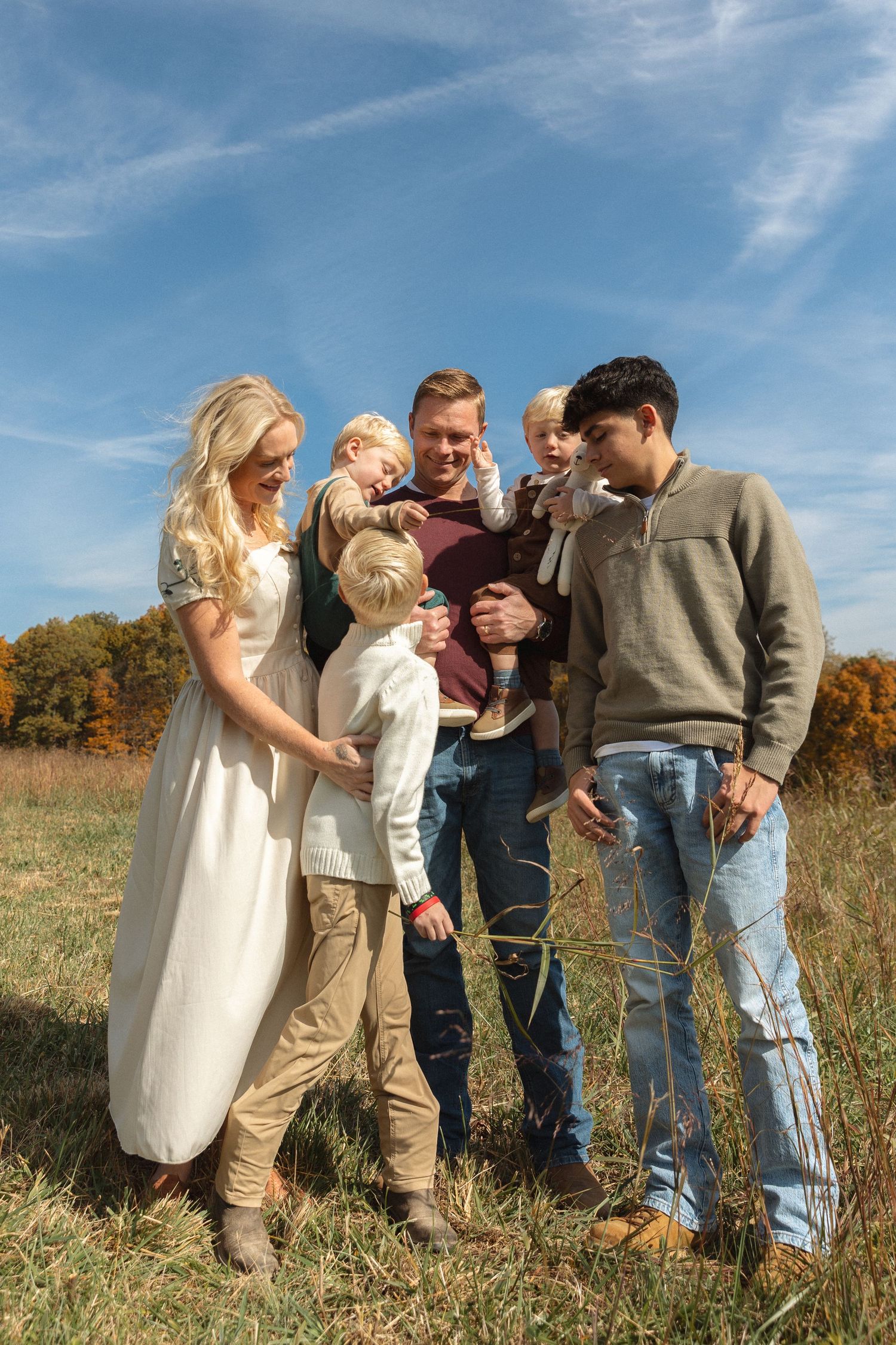 Blended family with three young children gathered together in an autumn field under blue sky.
