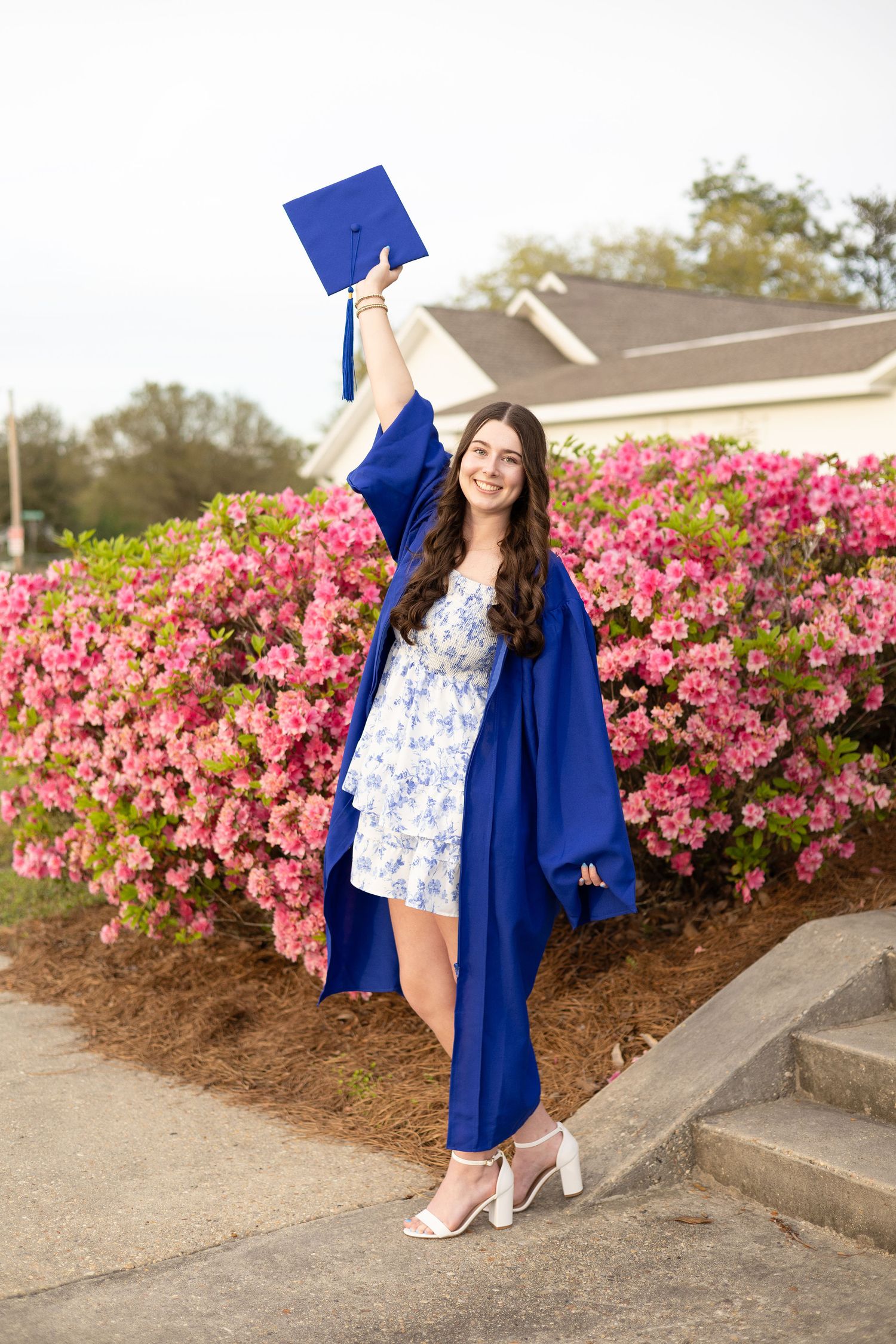 a high school graduate senior posing with her cap and gown in front of azaleas