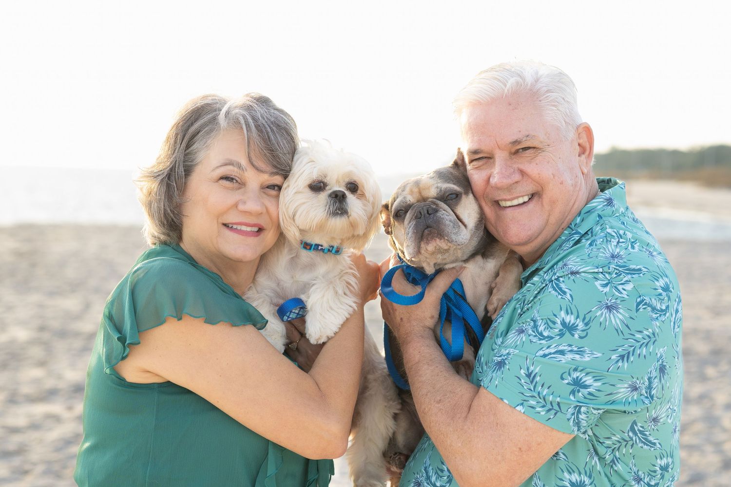 an older couple posing with their two small dogs on the beach