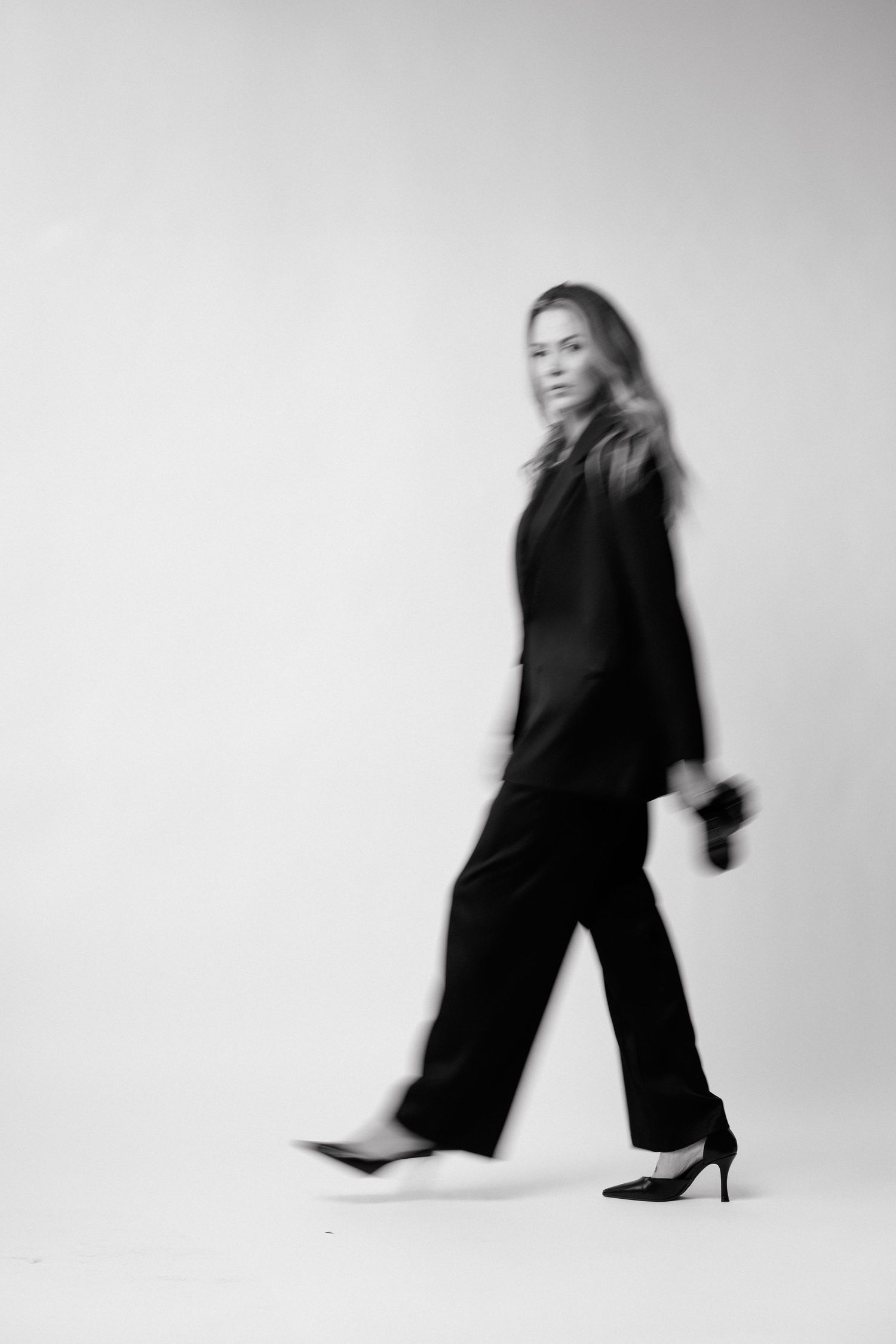 Black and white photo of a woman in a black suit walking with motion blur effect.
