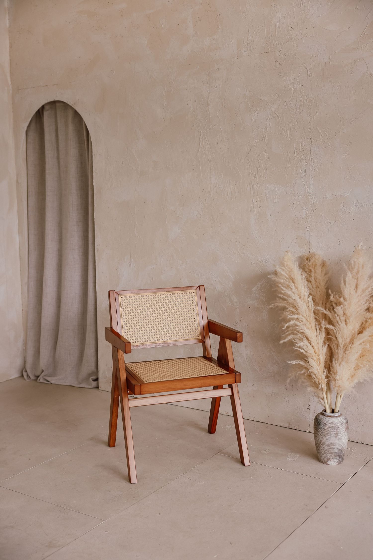 Minimalist boho room with rattan chair, pampas grass vase, arched niche, and neutral textured walls.