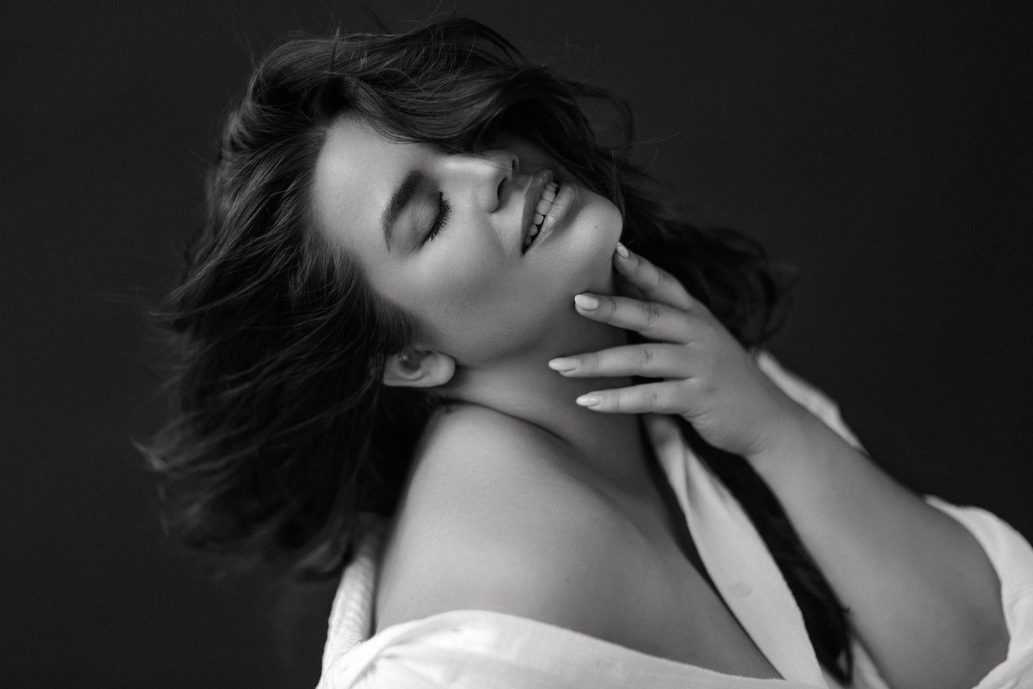 Black and white portrait of a woman with closed eyes, touching her neck gracefully, hair flowing softly.