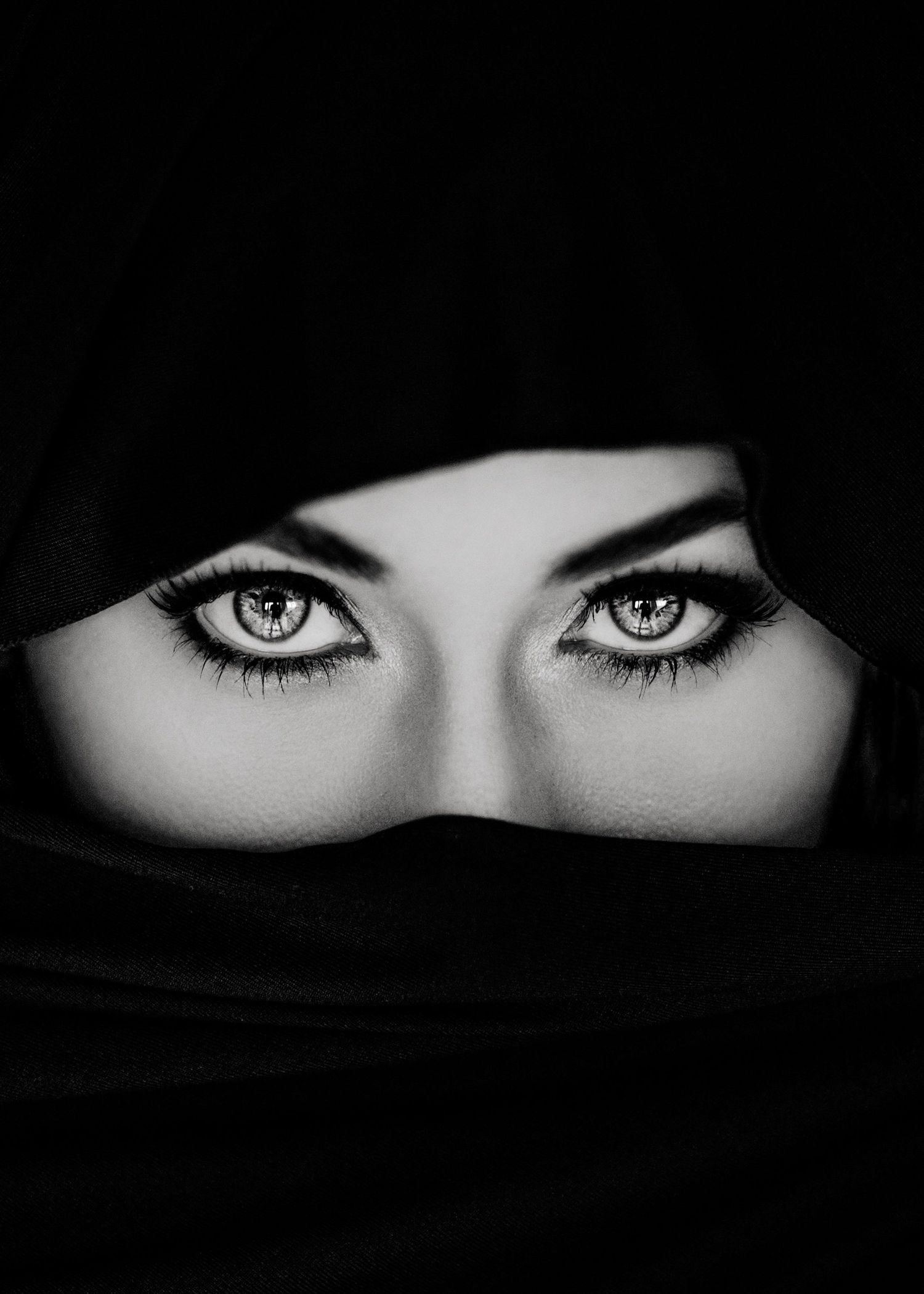 Black and white close-up of expressive eyes with dramatic lashes, framed by a dark niqab veil.