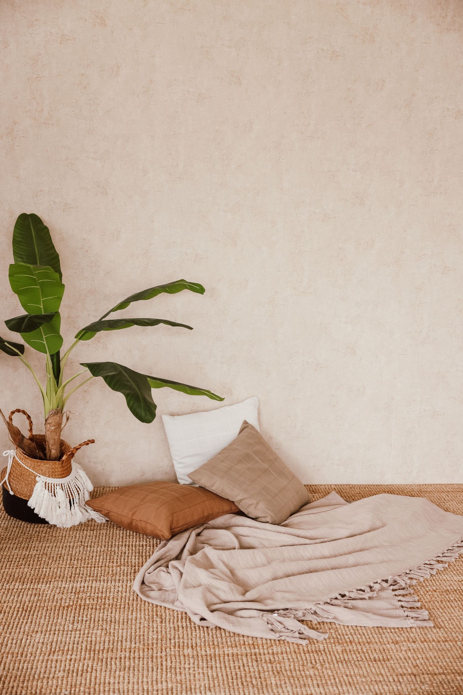 Boho living room corner with beige throw, neutral pillows, woven rug, and tropical plant in basket planter.